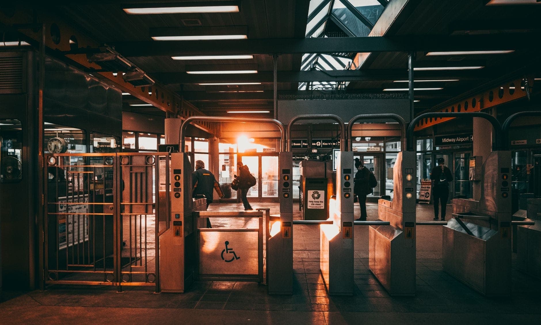 Des passagers franchissant les portillons d'une station de transit moderne avec la lumière du soleil en arrière-plan.