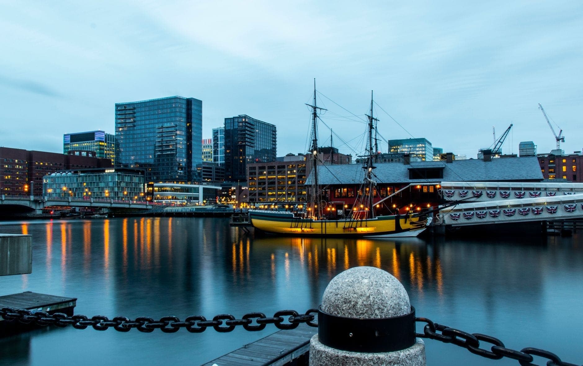 Réplique historique d'un navire amarré au Boston Tea Party Ships & Museum sur le Fort Point Channel, avec la skyline de la ville en arrière-plan au crépuscule.