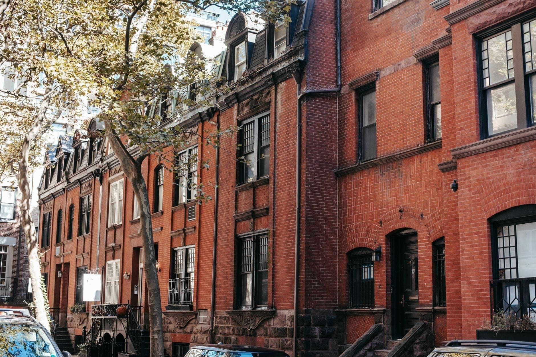 Rangée de maisons de ville historiques en grès brun avec des arbres et des voitures garées le long d'une rue résidentielle de Boston.