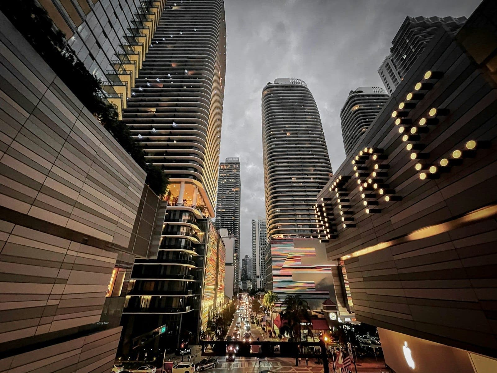 Modern high-rise towers and illuminated building signs line a busy street in Brickell, Miami's vibrant urban financial district at dusk.