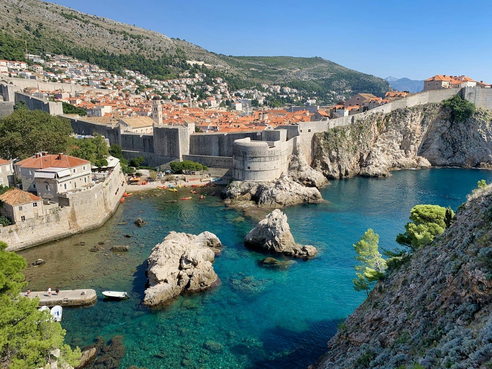Vista clara y luminosa de las antiguas murallas, acantilados y mar turquesa de Dubrovnik en buen tiempo, mostrando el paisaje costero cerca de Buza Bar.