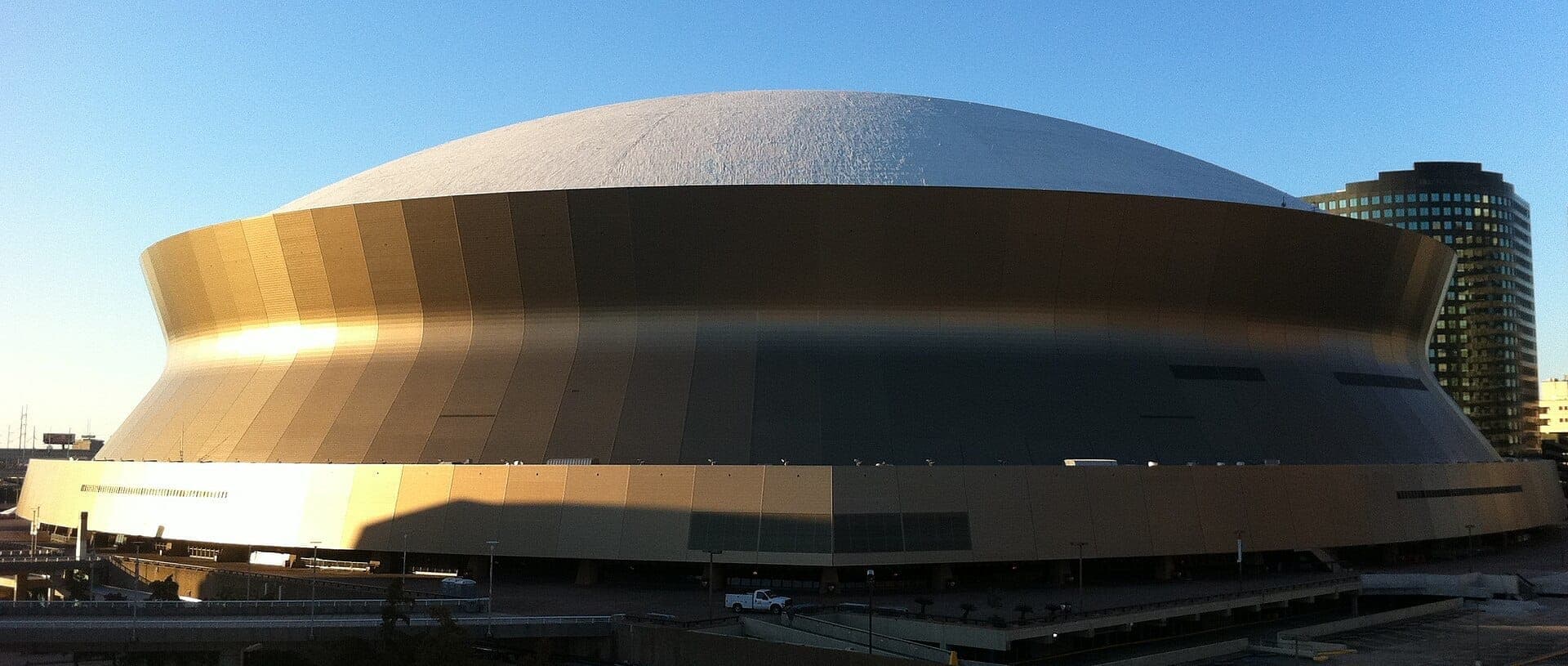 The iconic golden exterior of Caesars Superdome in New Orleans, shown under a clear blue sky with city buildings in the background.