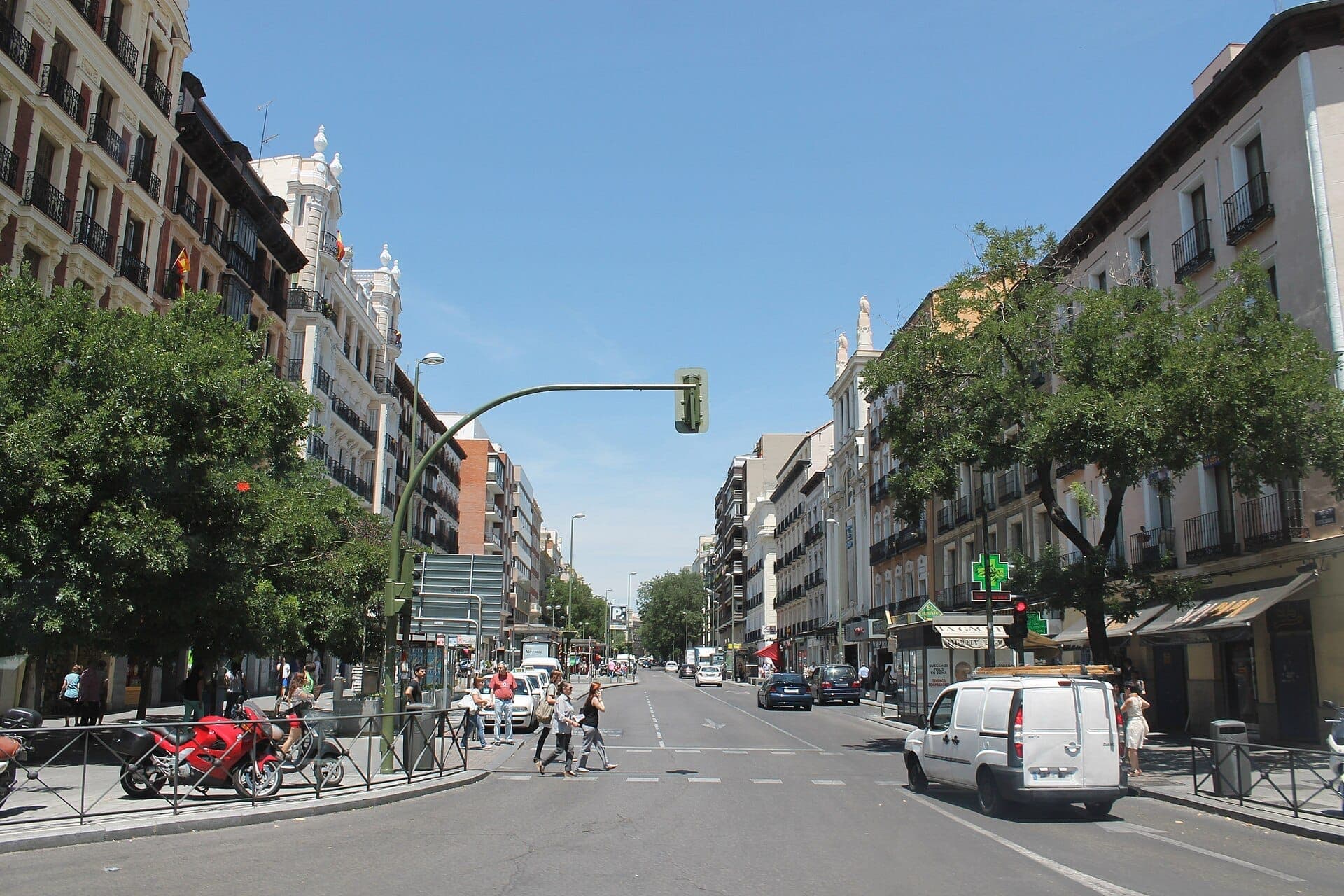 วิวของ Calle de Fuencarral ในมาดริดพร้อมอาคารประวัติศาสตร์ การจราจรบนถนน ต้นไม้ และคนเดินเท้าในวันที่แดดออก
