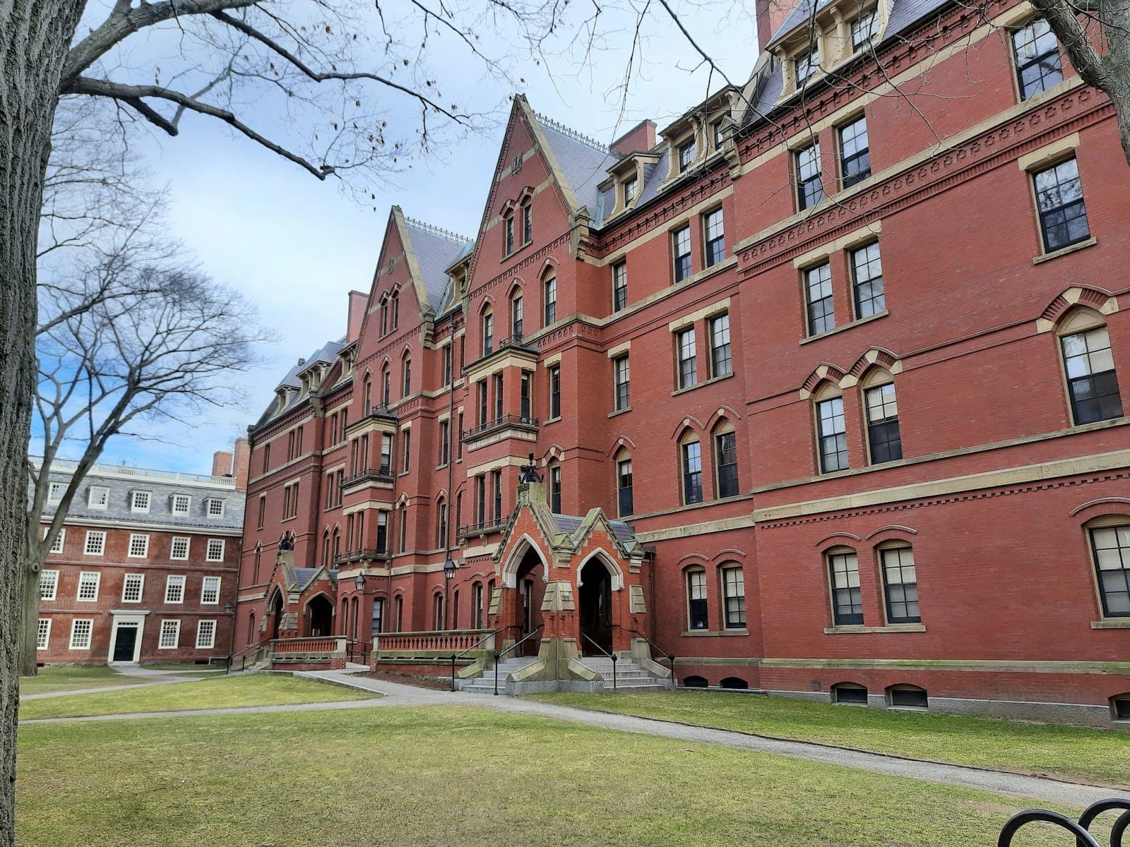 Bâtiment historique en briques rouges dans Harvard Yard par une journée claire, avec des pelouses verdoyantes et des allées ombragées, symbole de l'atmosphère emblématique de cette université d'élite à Cambridge.