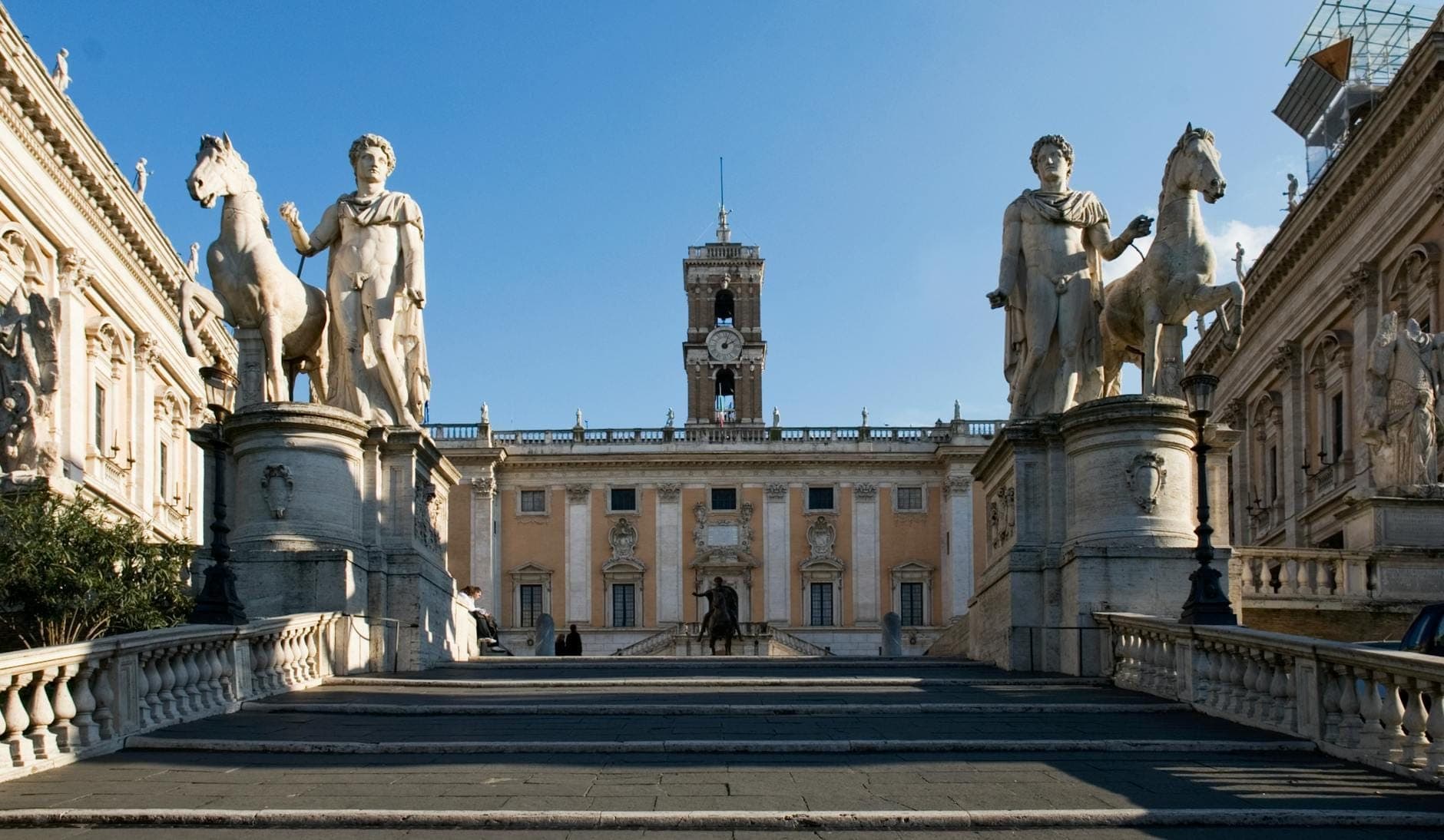 Ang malawak na hagdanan at mga estatwa na nagdadala pataas sa Piazza del Campidoglio sa Capitoline Hill, na may palazzo ni Michelangelo at maliwanag na asul na langit sa likod.