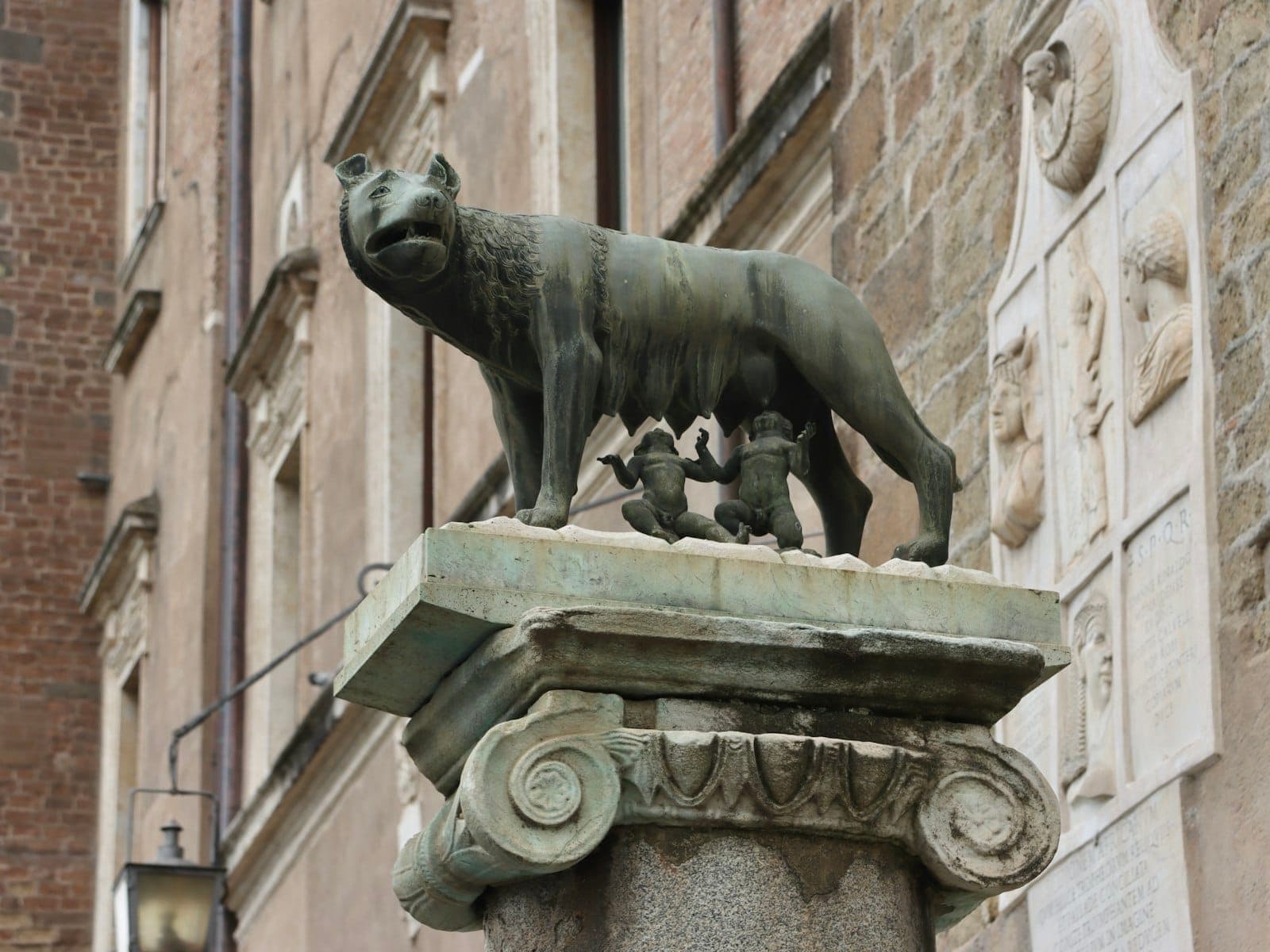 Estatwa na gawa sa tanso ng lobo na nagpapasuso kina Romulus at Remus, na itinatampok sa labas ng Capitoline Museums laban sa mga makasaysayang pader ng bato sa Roma.