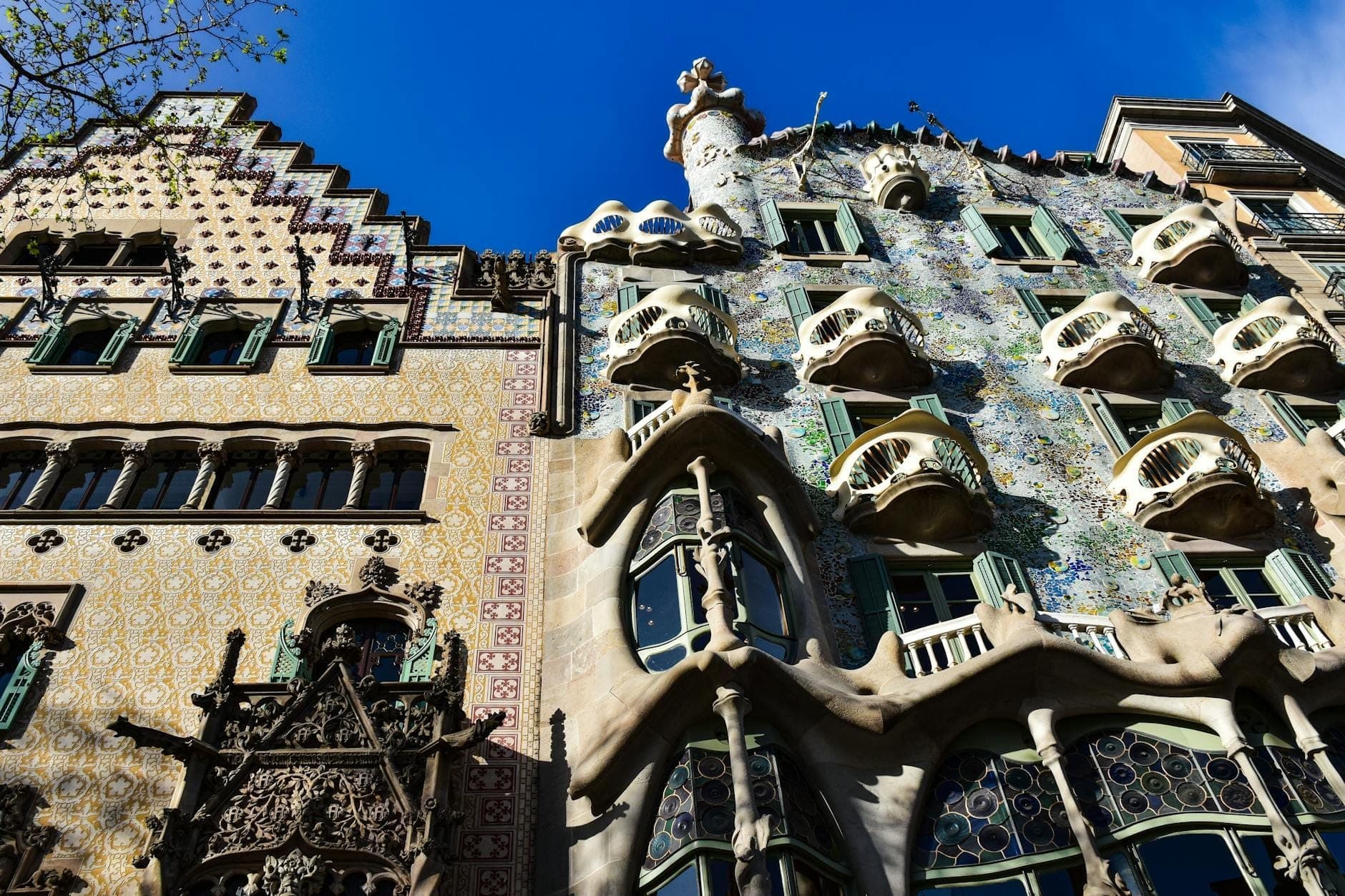 ด้านหน้าอาคาร Casa Batlló ในบาร์เซโลนา ประดับด้วยกระเบื้องเซรามิกหลากสี ระเบียงรูปกระดูก และหลังคาประติมากรรมสุดอลังการภายใต้ท้องฟ้าสีฟ้าสดใส