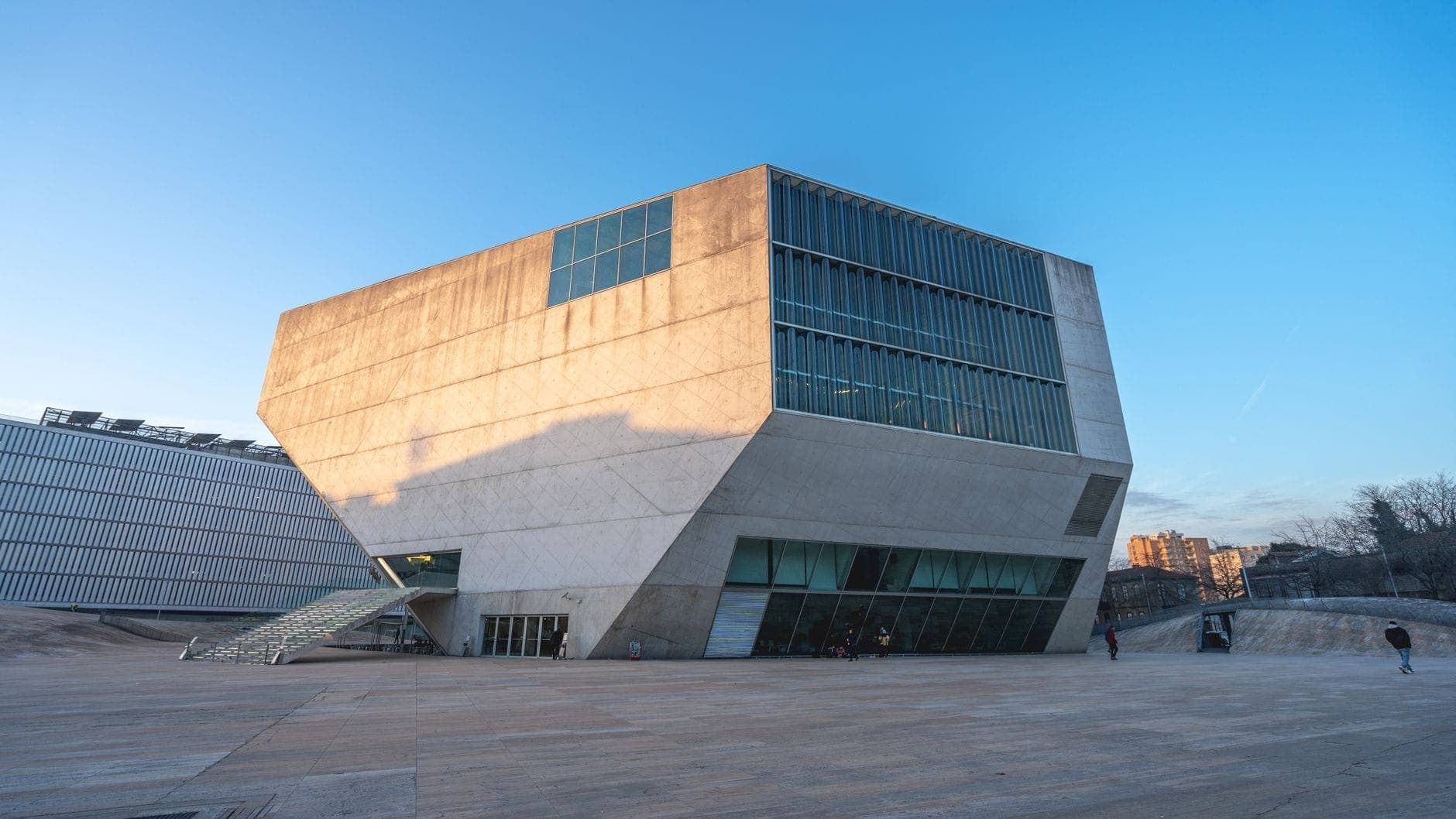 Vista grandangolare della Casa da Música a Porto al tramonto, con la sua spettacolare forma geometrica in cemento bianco e le pareti in vetro, la piazza deserta e il cielo blu.