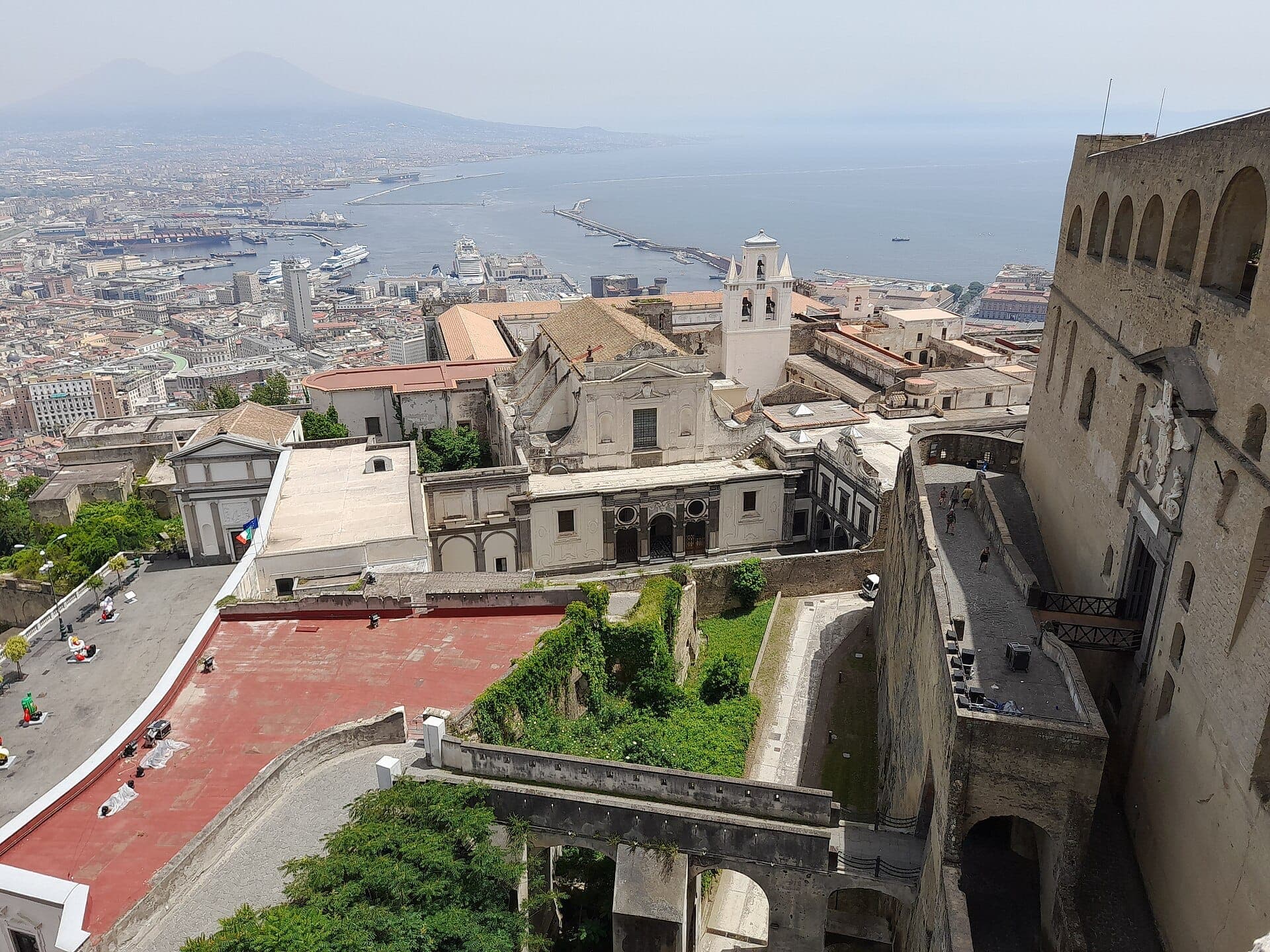 Vista do Castel Sant'Elmo com Nápoles, a baía e o Monte Vesúvio ao fundo em um dia claro, com as muralhas da fortaleza em primeiro plano.