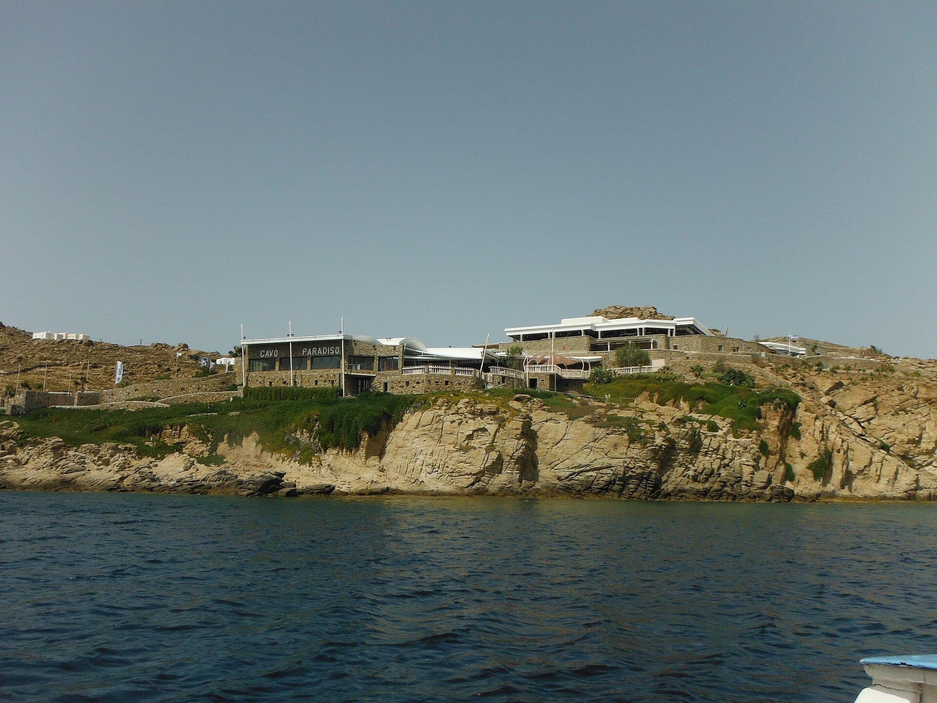 Cavo Paradiso Club Mykonos thront auf einem felsigen Klippenvorsprung über dem Ägäischen Meer mit seinen Steingebäuden und dem strahlend blauen Himmel.
