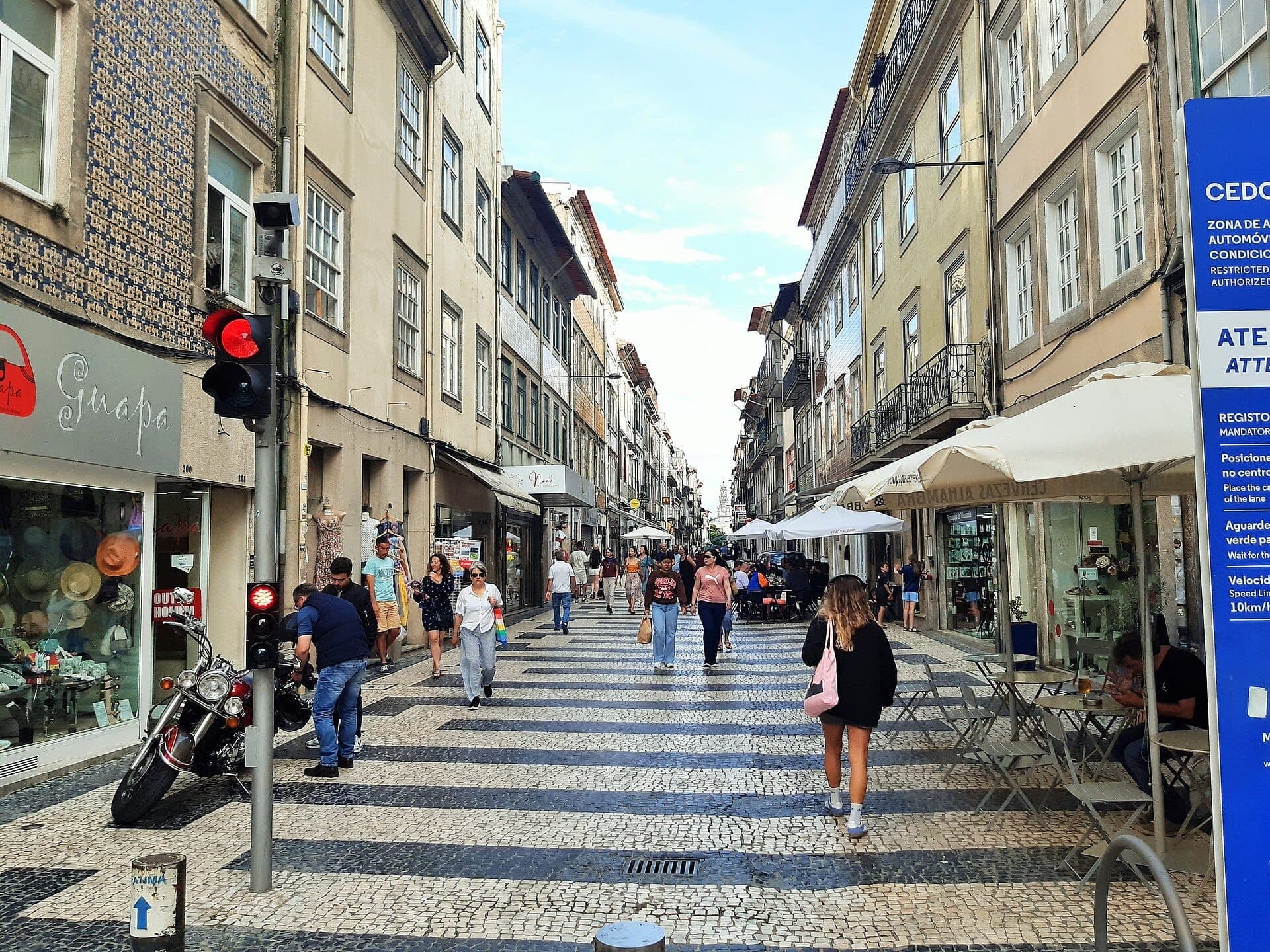 Jalan pejalan kaki di Cedofeita, Porto, dengan orang-orang berjalan di antara bangunan bersejarah, toko independen, dan kafe luar ruangan pada hari yang cerah.