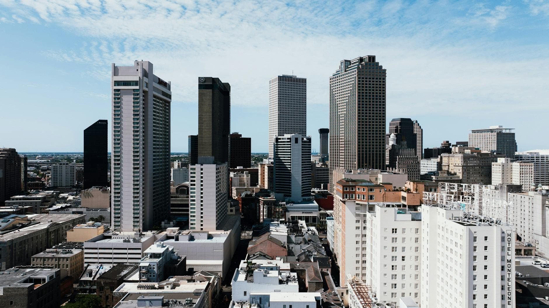Skyline of downtown New Orleans with modern glass office towers and historic brick buildings in the Central Business District under a bright blue sky.