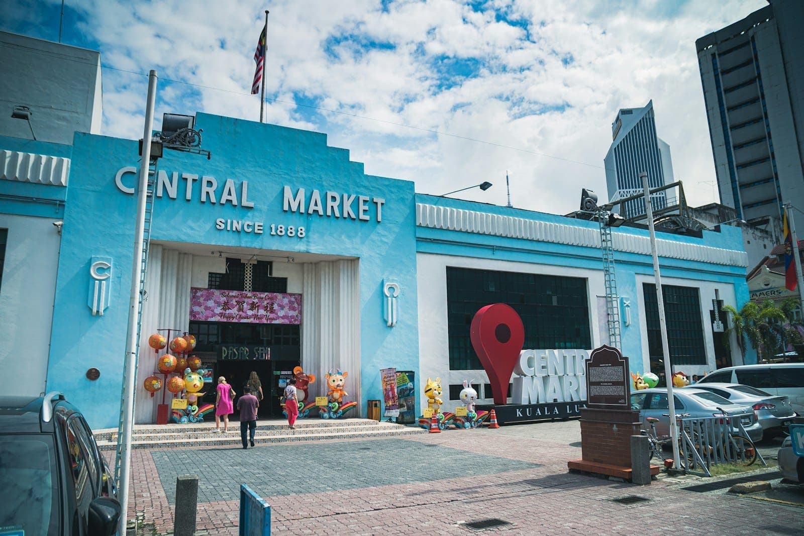 Mavi Art Deco cephesi, giriş tabelası ve Pasar Seni miras pazarındaki ziyaretçileriyle Kuala Lumpur Central Market'ın dış görünümü