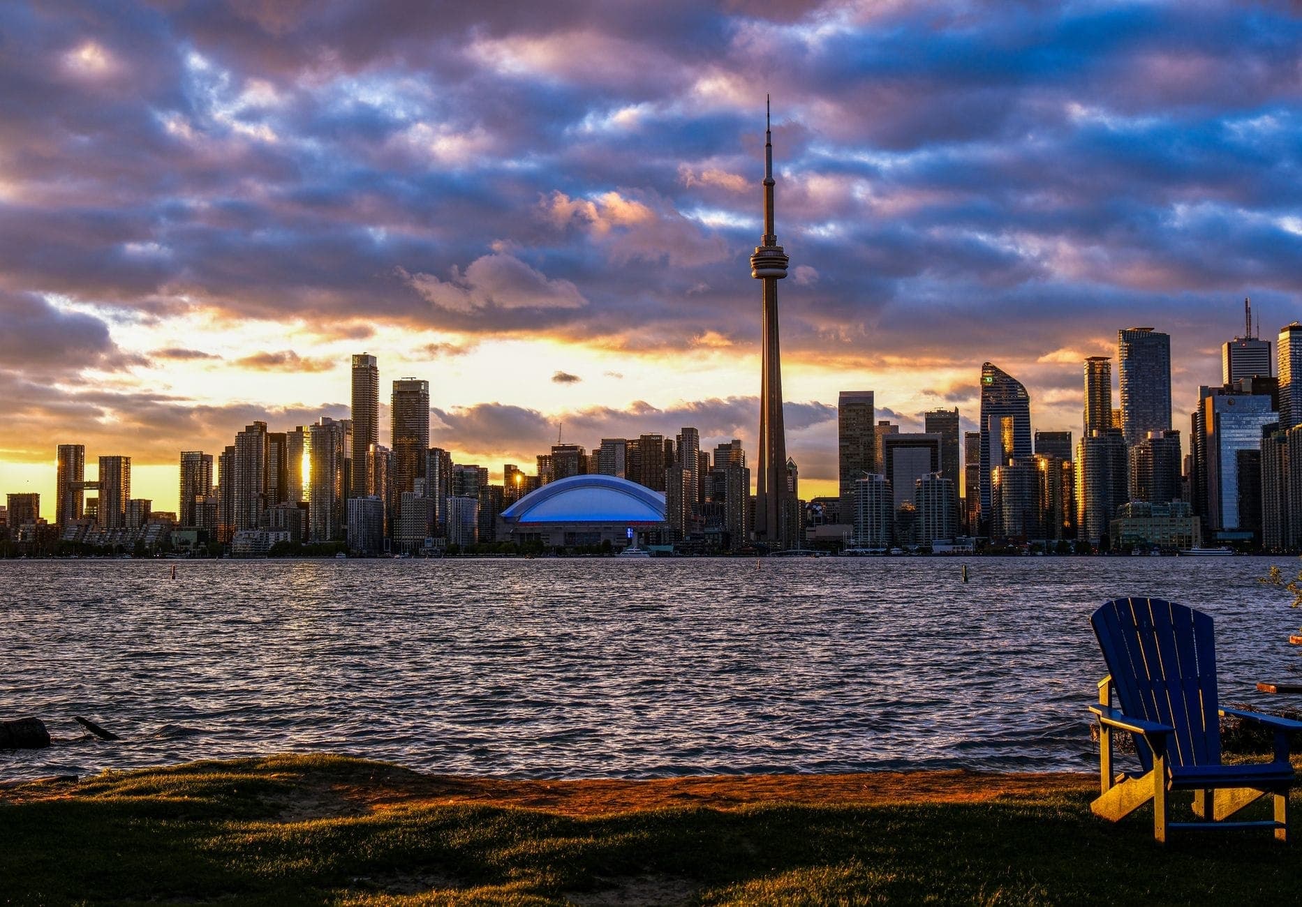 Vista da Centre Island al tramonto con lo skyline di Toronto, la CN Tower, il lungomare e sedie Adirondack in primo piano.