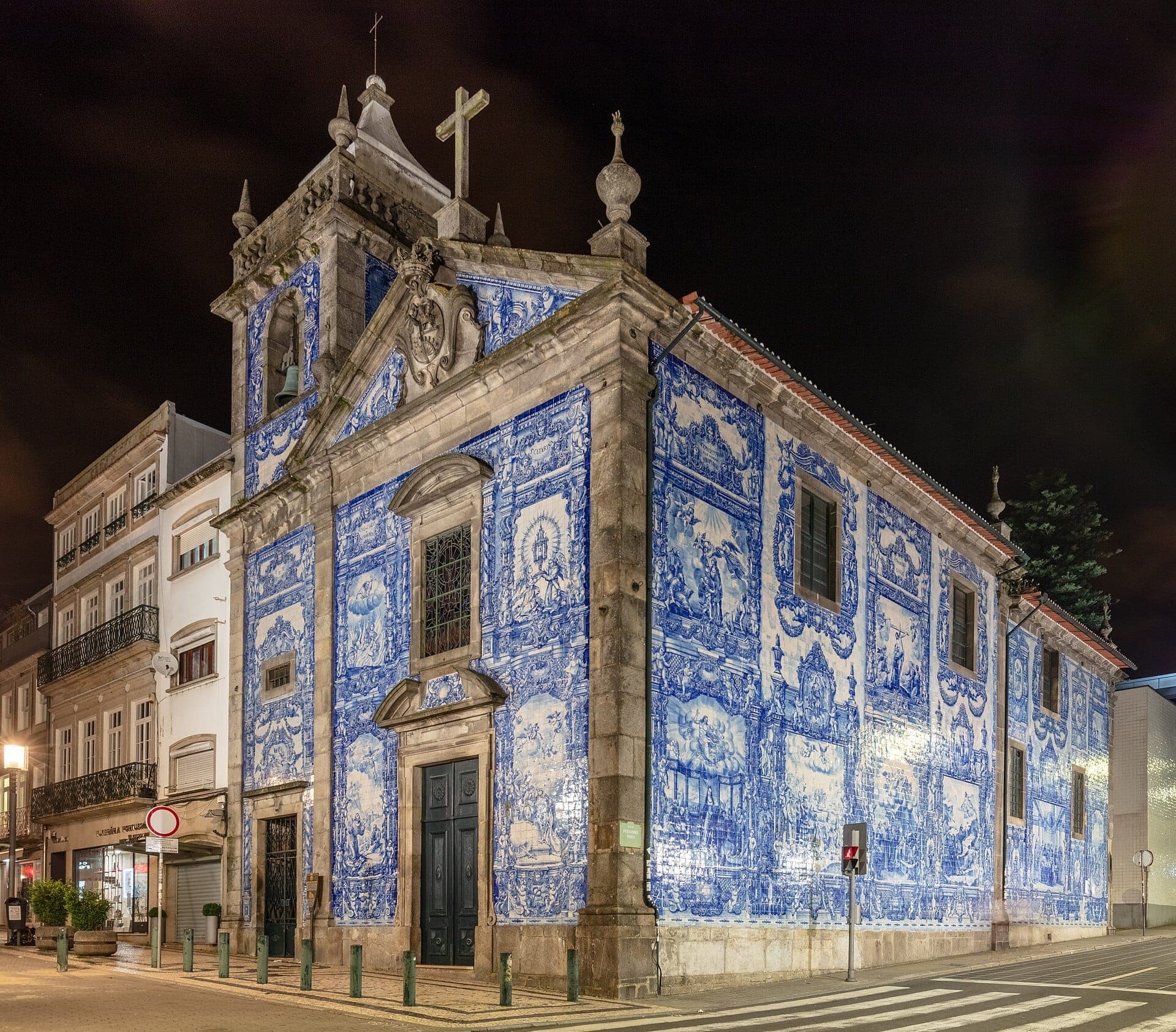 Die Capela das Almas in Porto bei Nacht beleuchtet, mit ihren lebhaften blau-weißen Azulejo-Kacheln und barocken Architekturdetails an einer Straßenecke.