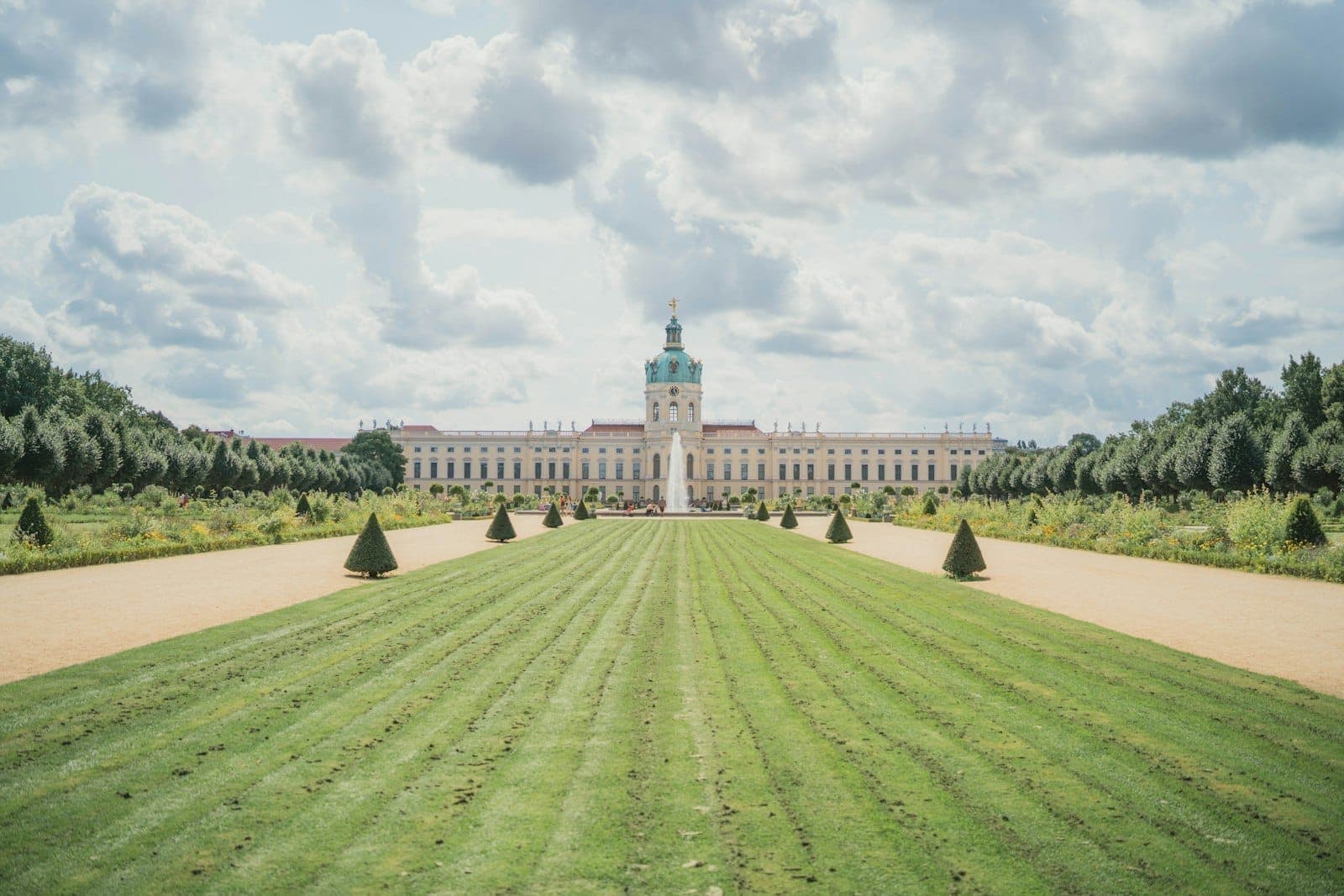 มุมกว้างของพระราชวัง Charlottenburg สนามหญ้าเรียบเรียง ทางเดินสมมาตร มีต้นไม้และท้องฟ้ามีเมฆบางส่วนในเบอร์ลิน