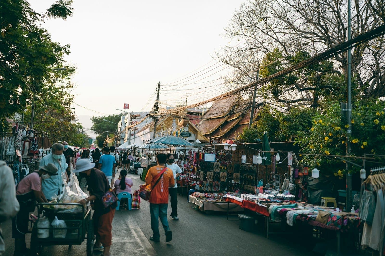 Tętniąca życiem scena targu na świeżym powietrzu w Chiang Mai z ludźmi przeglądającymi stragany i dachami świątyń widocznymi w tle.