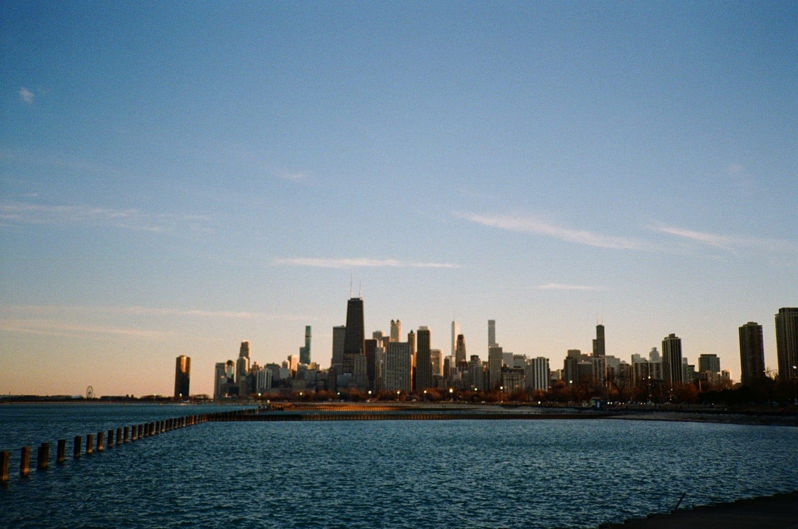 Chicago lakefront at dusk with a clear view of city skyline, gently lit waterfront, and calm water in the foreground.