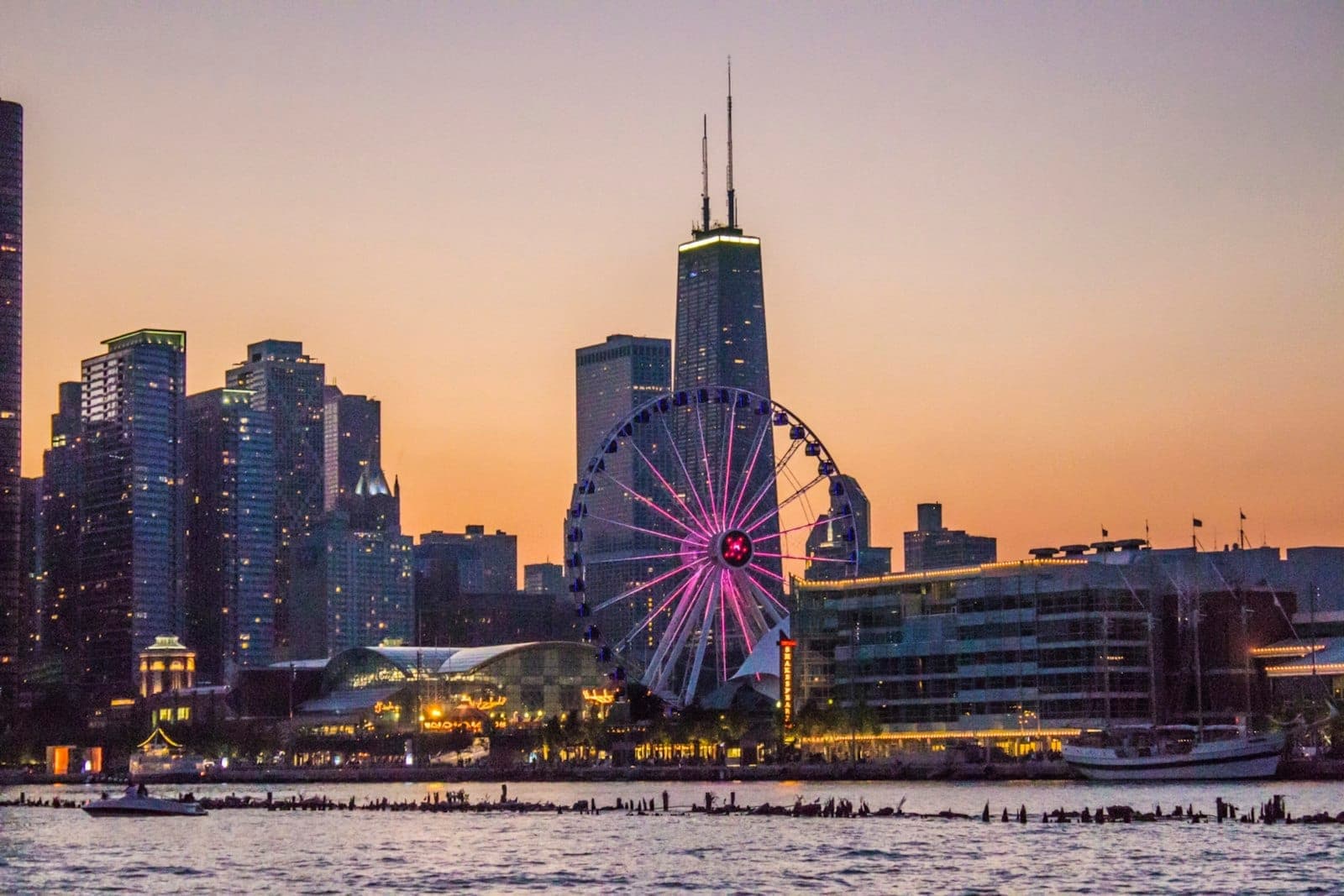 Navy Pier ferris wheel glowing at sunset with Chicago skyline and water in the foreground.