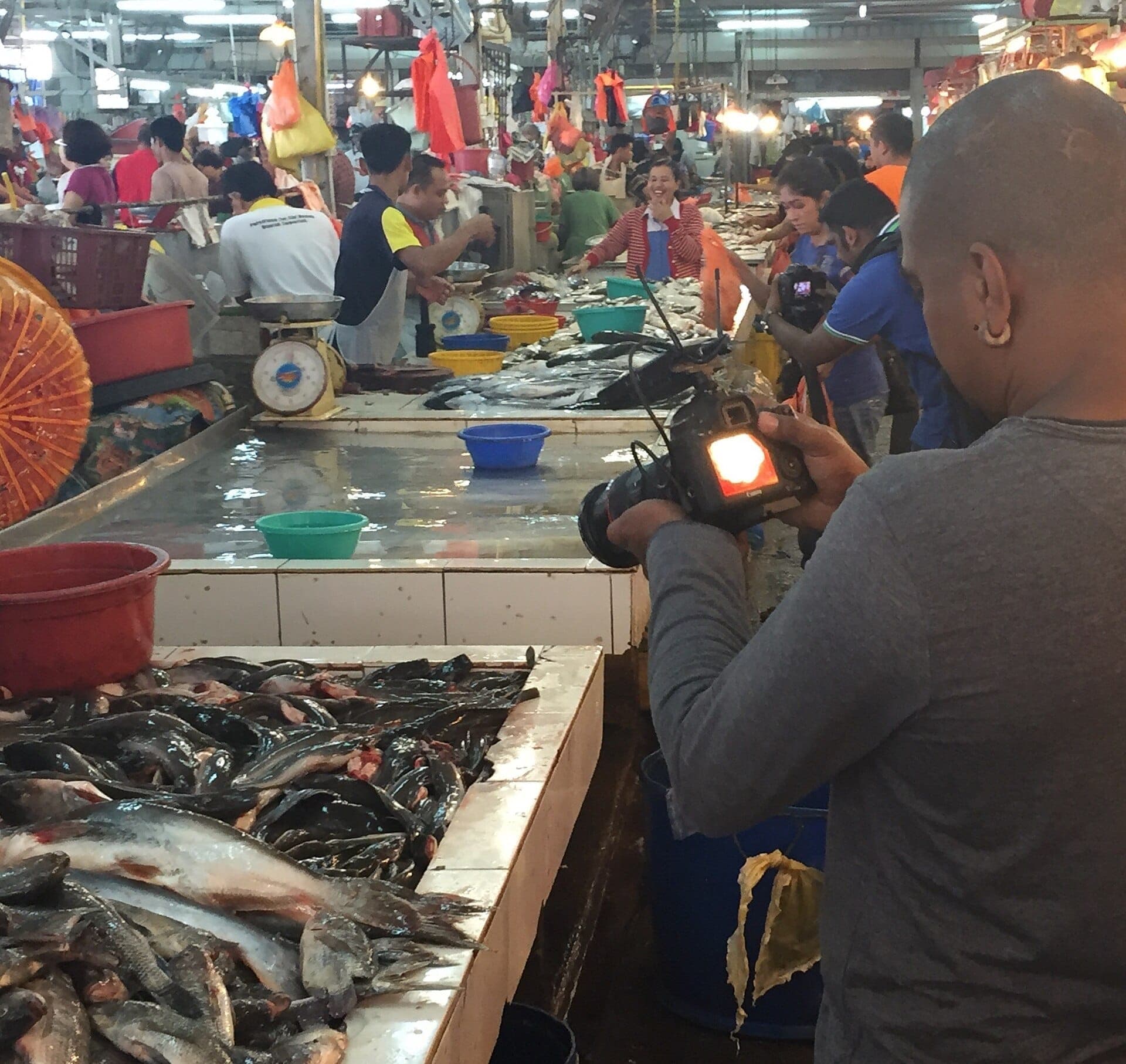 Poisson frais exposé au Chow Kit Market avec des vendeurs et des acheteurs sous les lumières vives du marché dans une atmosphère intérieure animée.