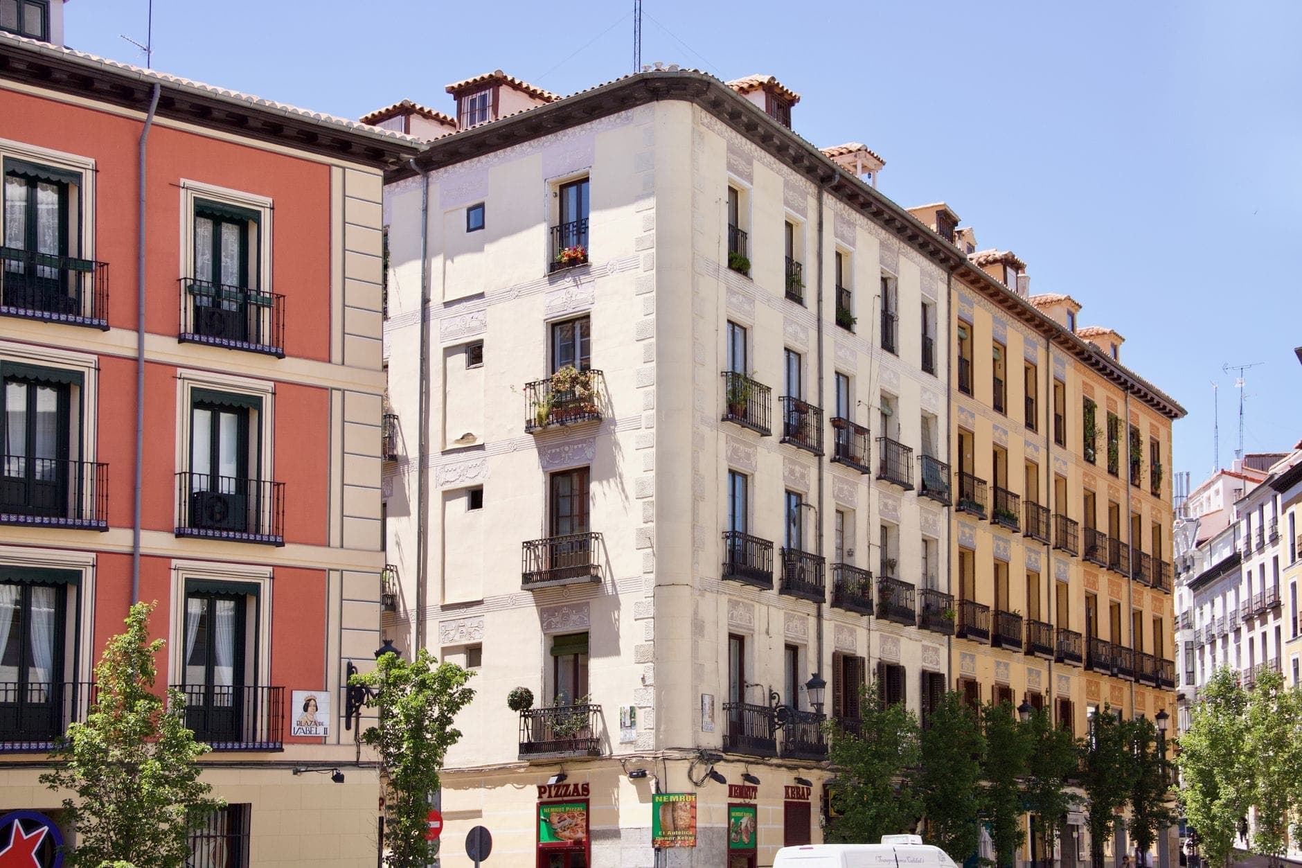 ถนนสุดคึกคักใน Chueca ใจกลางมาดริด รายล้อมด้วยอาคารเก่า ฟาซาดสีสด ระเบียงเหล็กดัด และต้นไม้เขียวขจีใต้ท้องฟ้าสีฟ้าสดใส