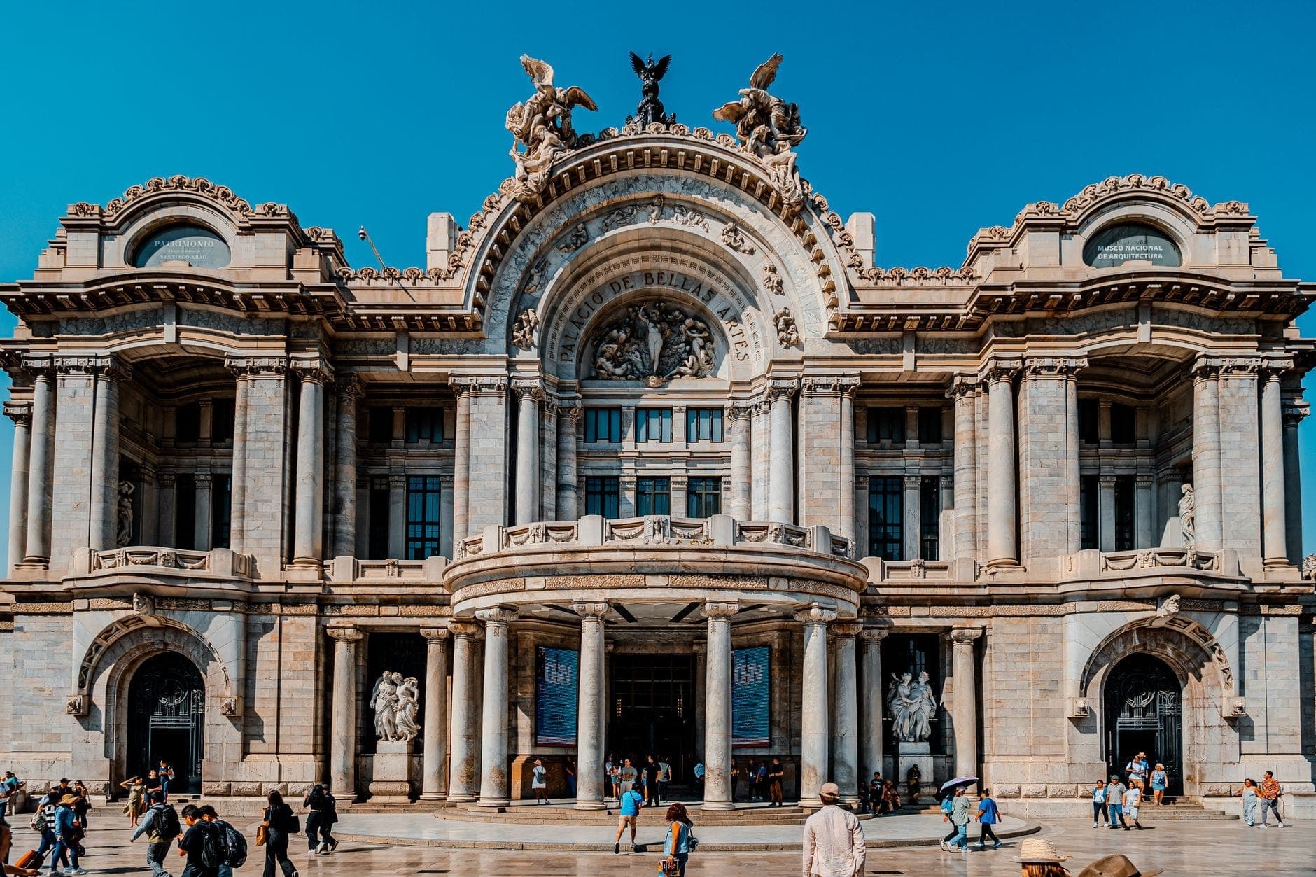 Широкий вид на богато украшенный фасад Círculo de Bellas Artes: прохожие идут по улице на фоне ярко-синего мадридского неба.
