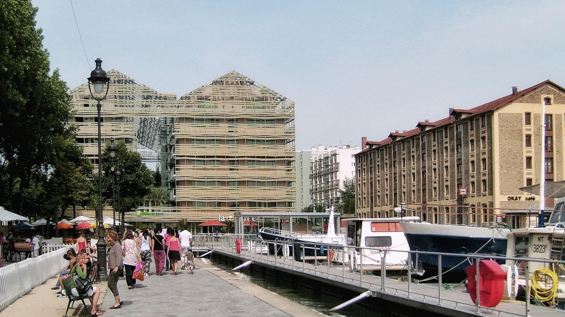 Exterior view of the Cité des Sciences et de l'Industrie glass-and-steel building along the canal with people walking and boats docked nearby.