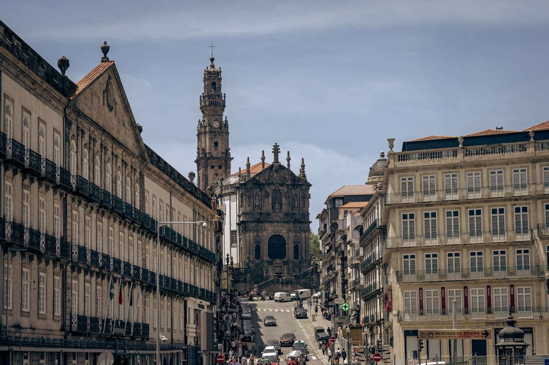 Straßenansicht der Clérigos-Kirche mit ihrem hohen barocken Glockenturm, der über die historischen Gebäude Portos aufragt – blauer Himmel, Menschen auf dem Bürgersteig.