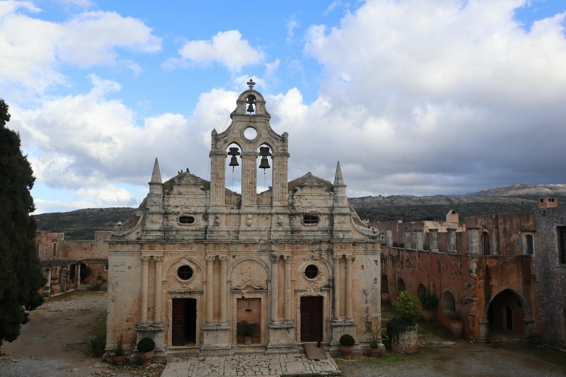 Storico monastero in pietra di Arkadi tra le colline cretesi, con tre campanili e uno spettacolare cielo nuvoloso sullo sfondo.