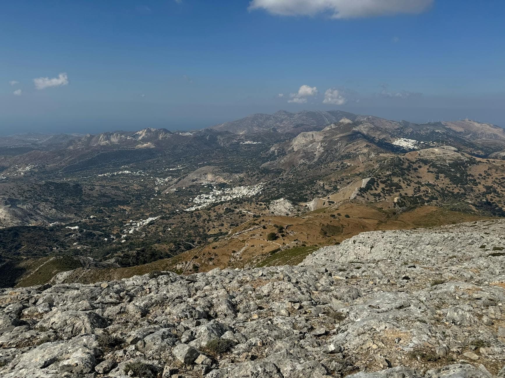 Paesaggio montano con villaggi sparsi e terreno accidentato sotto un cielo limpido, che evoca l'entroterra remoto dell'Altopiano di Lassithi a Creta.