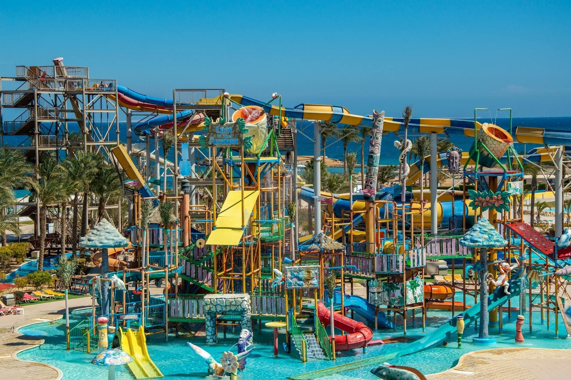 Heller, farbenfroher Wasserpark mit mehreren Rutschen, Planschbereichen und Spielstrukturen an einem sonnigen Tag in Meeresnähe.