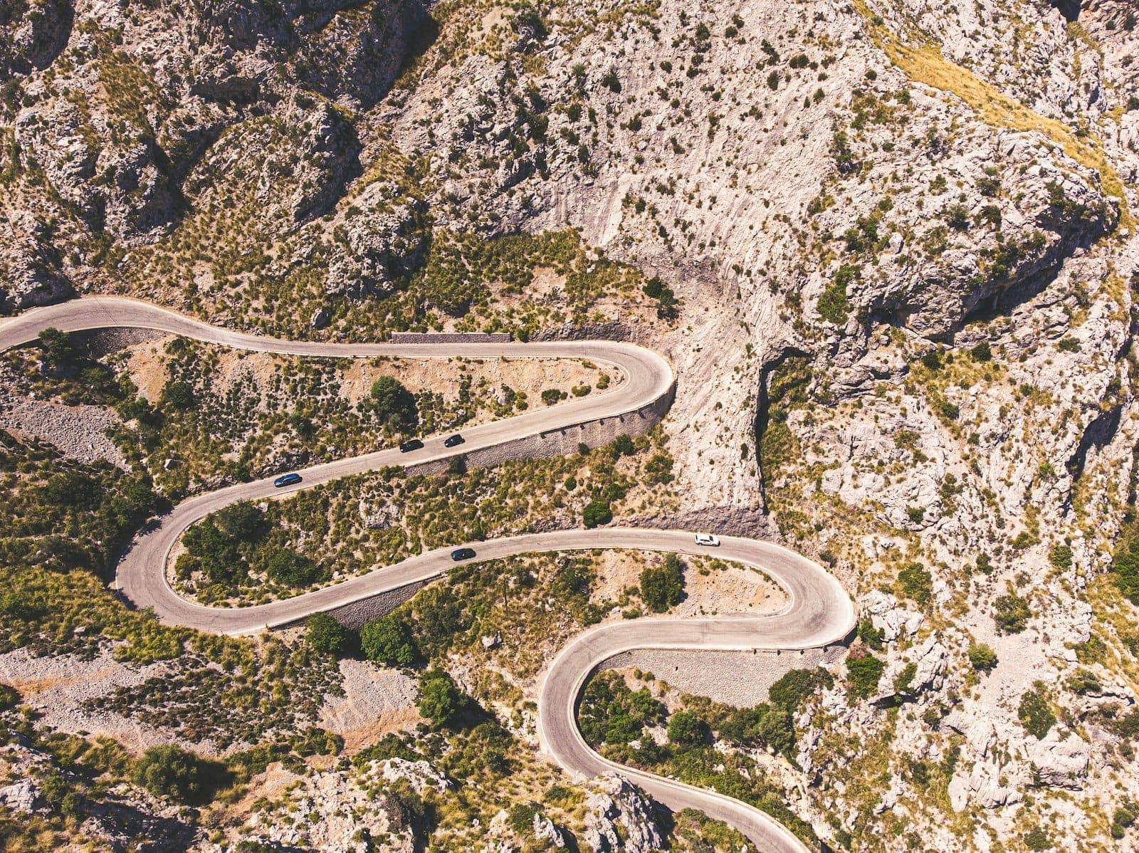 Mallorca'nın Tramuntana dağlarında kayalık araziden geçen sık virajlı kıvrımlı bir dağ yolunun havadan görünümü.