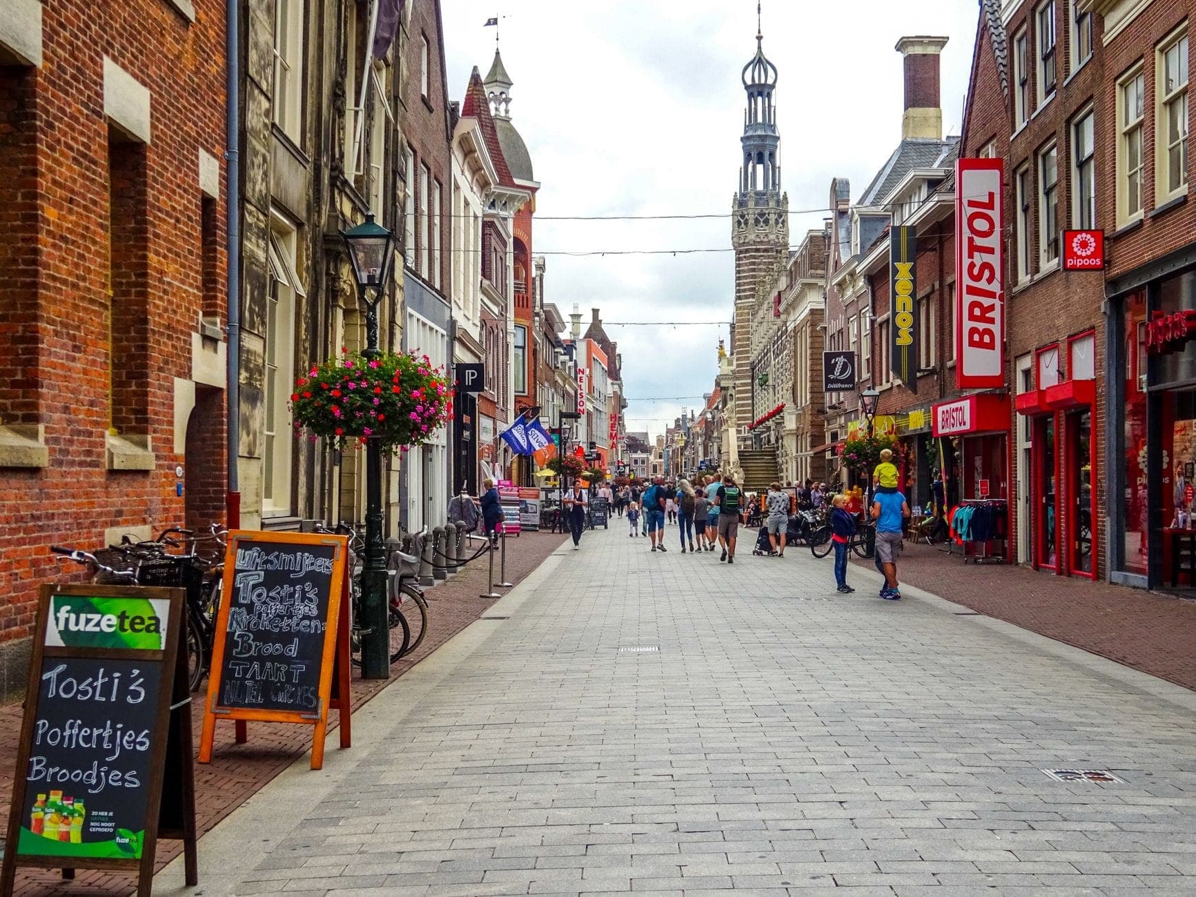 Belebte Fußgängerzone in Amsterdam, gesäumt von Geschäften, Cafés, Fahrrädern und Spaziergängern unter historischer niederländischer Architektur.
