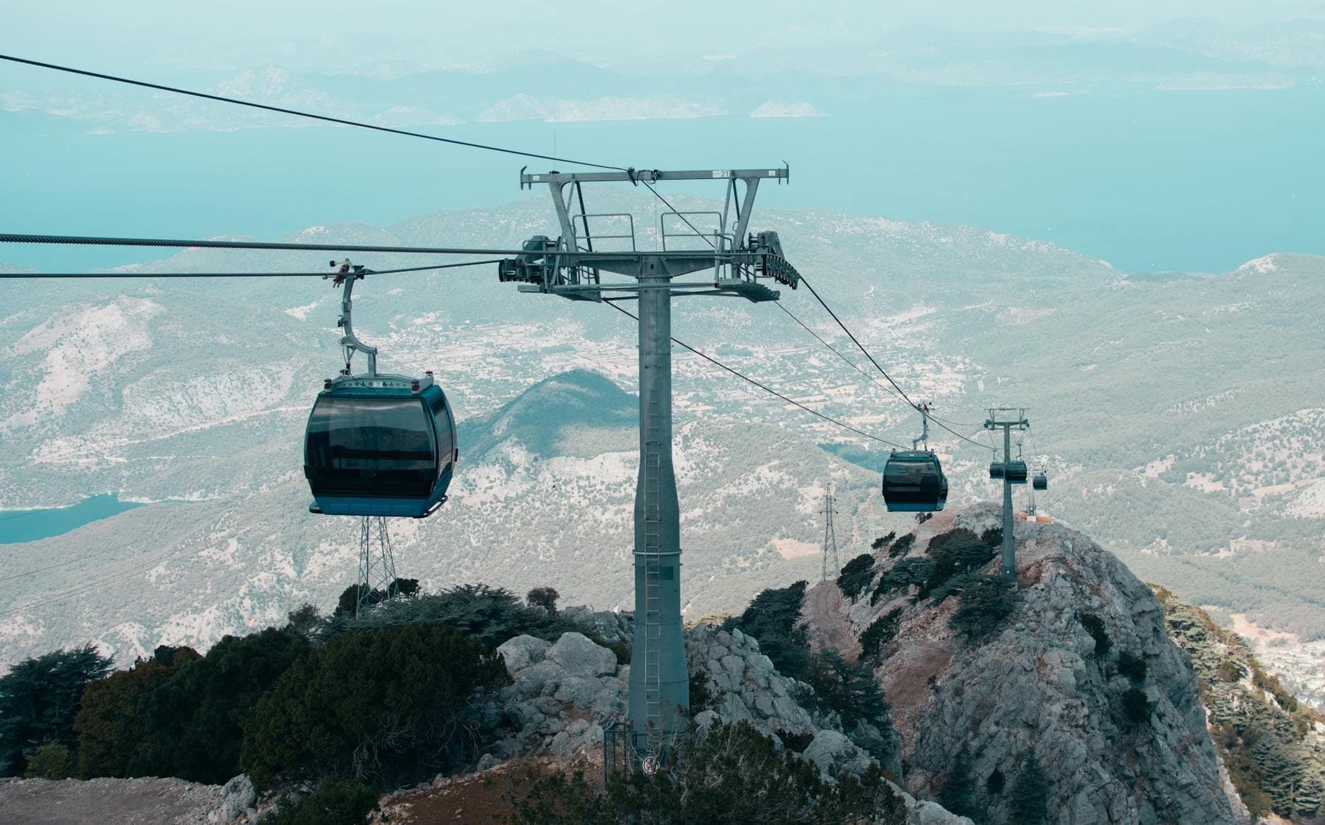 Téléphériques montant au-dessus d'un paysage montagneux avec vue sur la mer et terrain accidenté près d'Antalya, idéal pour l'aventure et les expériences uniques.