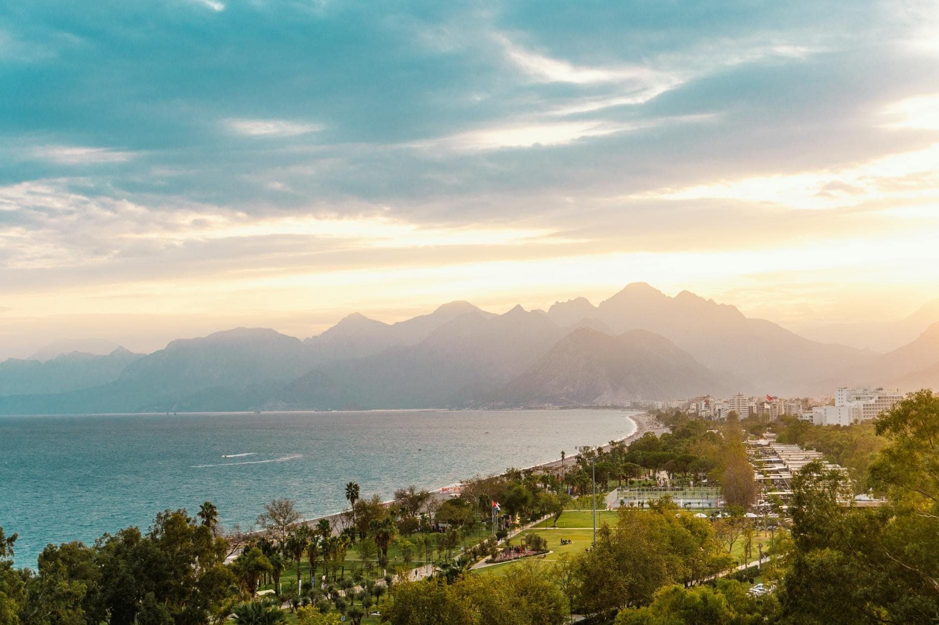 Malerischer Blick auf die Küste von Antalya bei Sonnenuntergang mit dramatischen Bergen, üppigem Grün und dem Mittelmeer unter einem farbenprächtigen Himmel.