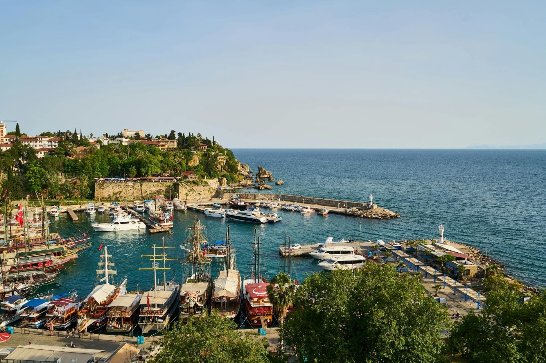 Port pittoresque à Antalya avec des bateaux, des yachts et des bâtiments historiques de la vieille ville sur une falaise au bord de la mer Méditerranée sous un ciel dégagé.