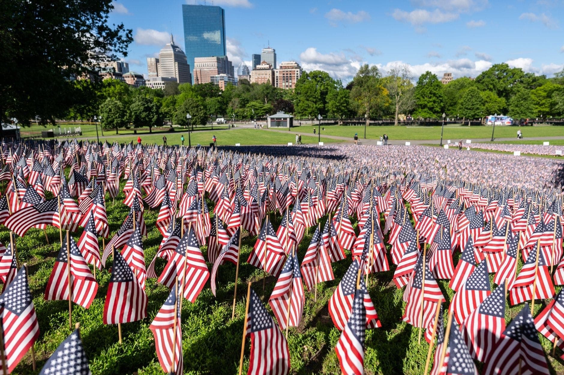 Des centaines de drapeaux américains plantés sur Boston Common avec les gratte-ciel du centre-ville de Boston et des arbres verts visibles par une journée ensoleillée.
