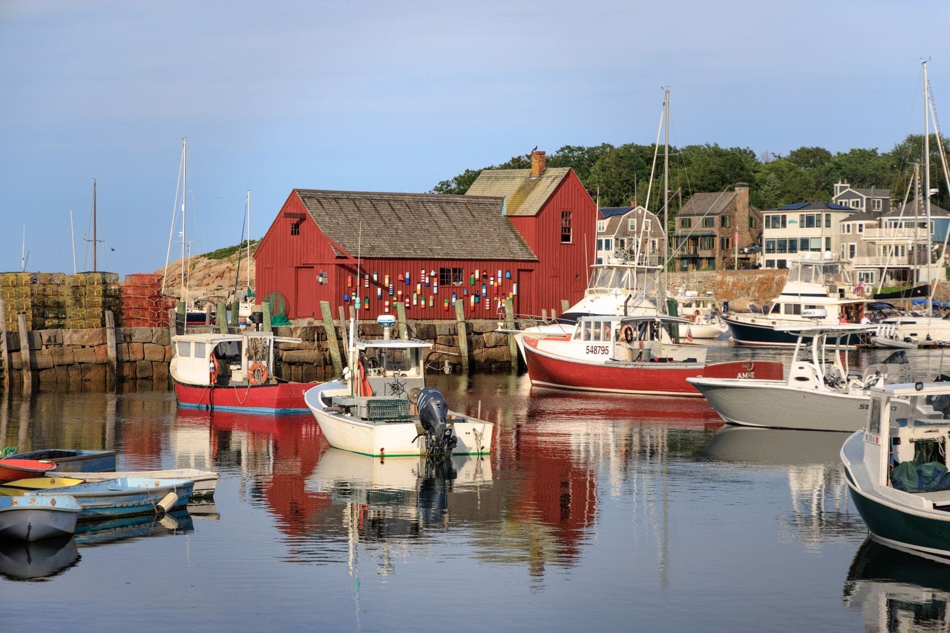 Pittoresque scène de port dans une ville côtière de Nouvelle-Angleterre avec une cabane de pêche rouge, des casiers à homard, des bateaux et l'eau reflétant bâtiments et embarcations.