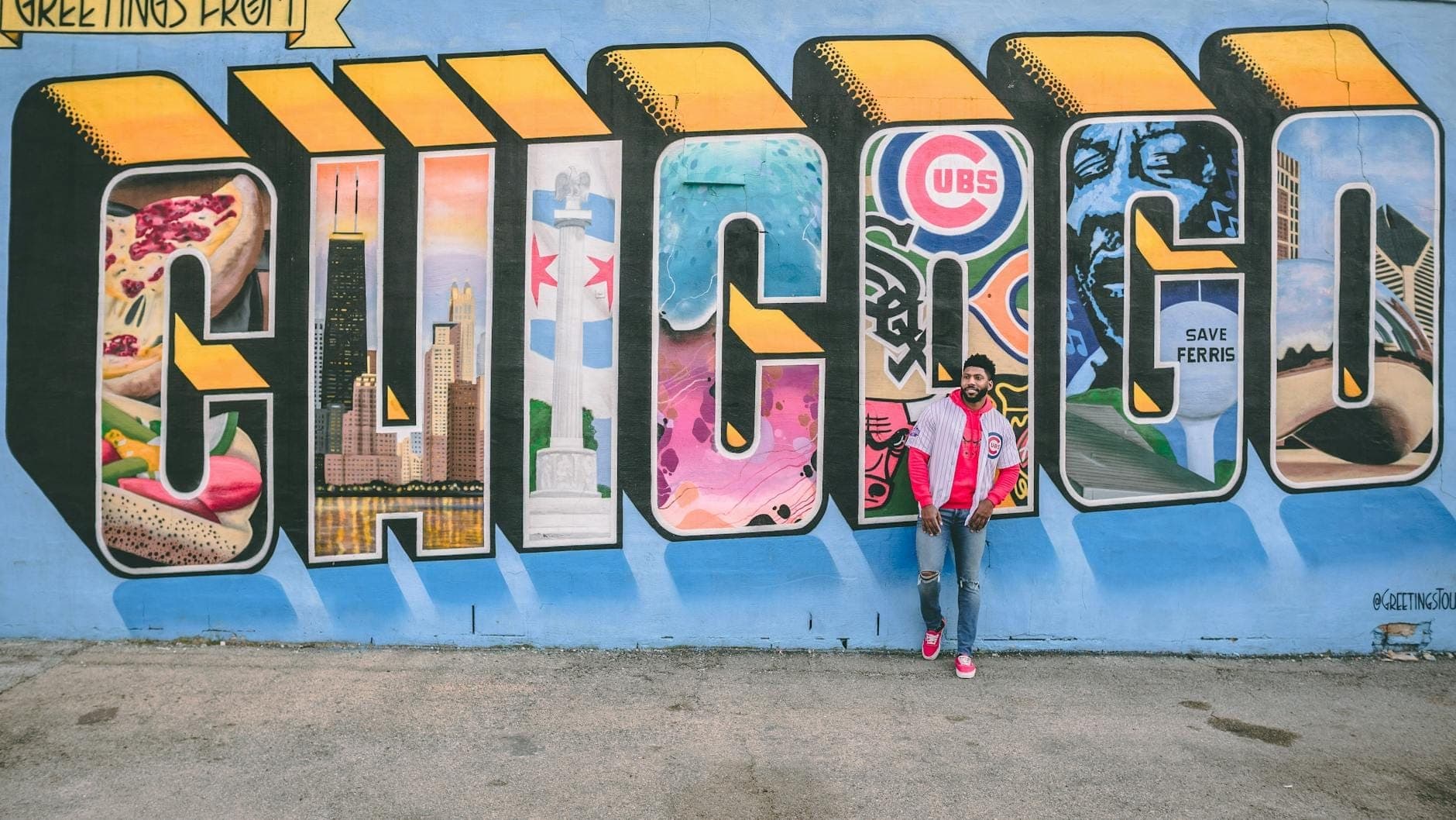 Persona de pie frente a un gran mural con la palabra 'CHICAGO', imágenes icónicas de la ciudad y símbolos sobre una pared azul.