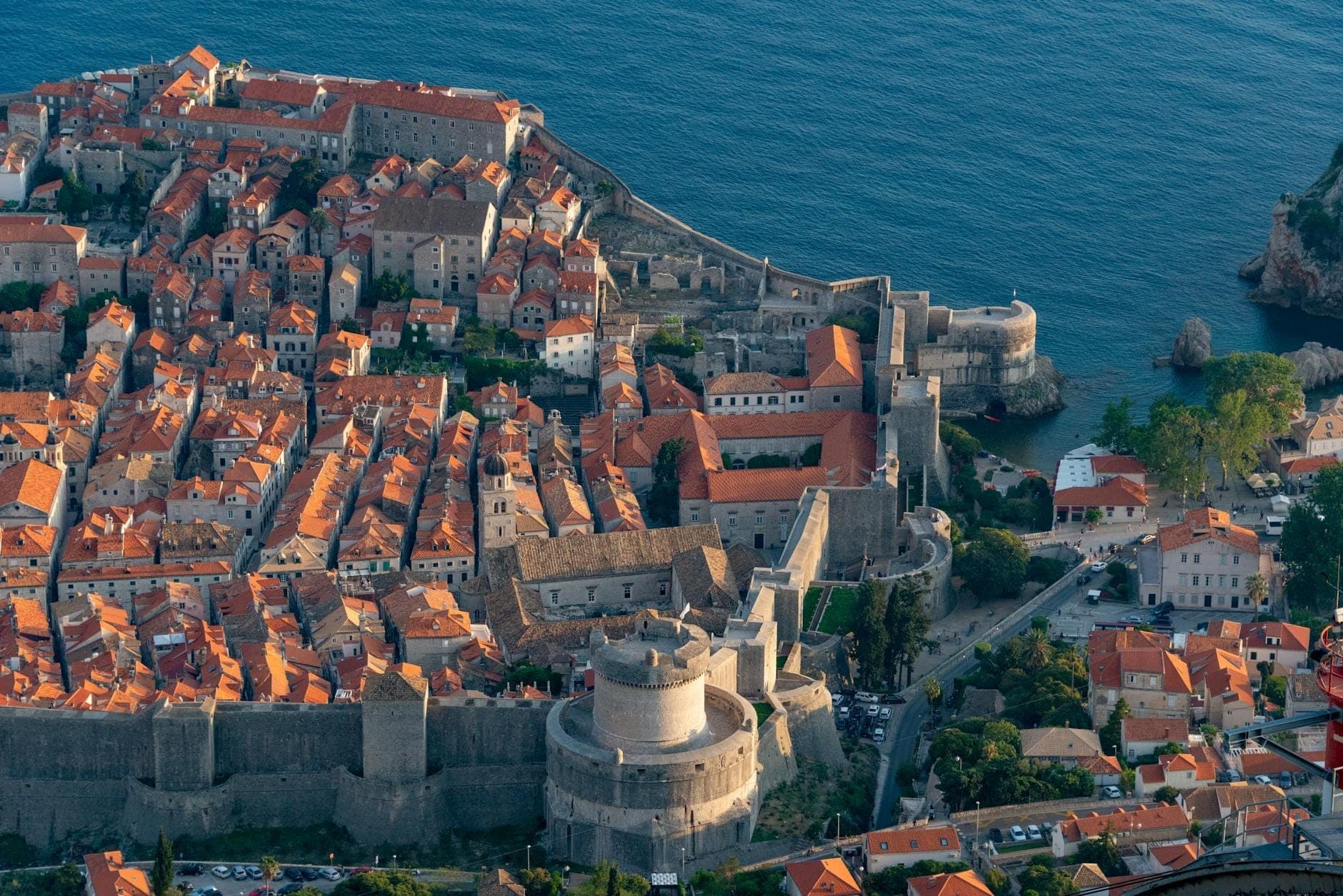 Vue aérienne de la vieille ville fortifiée de Dubrovnik avec ses fortifications en pierre, ses toits de tuiles rouges et le littoral environnant par une journée ensoleillée.