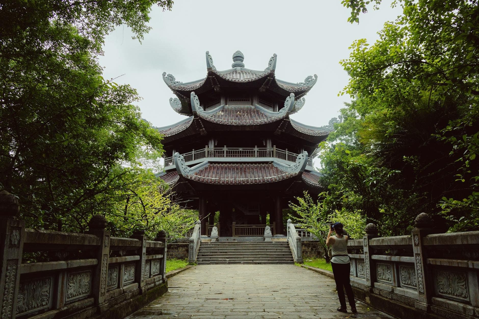 Pagode bouddhiste traditionnelle à plusieurs niveaux entourée d'une végétation luxuriante, avec un visiteur marchant le long d'un chemin en pierre menant au temple.