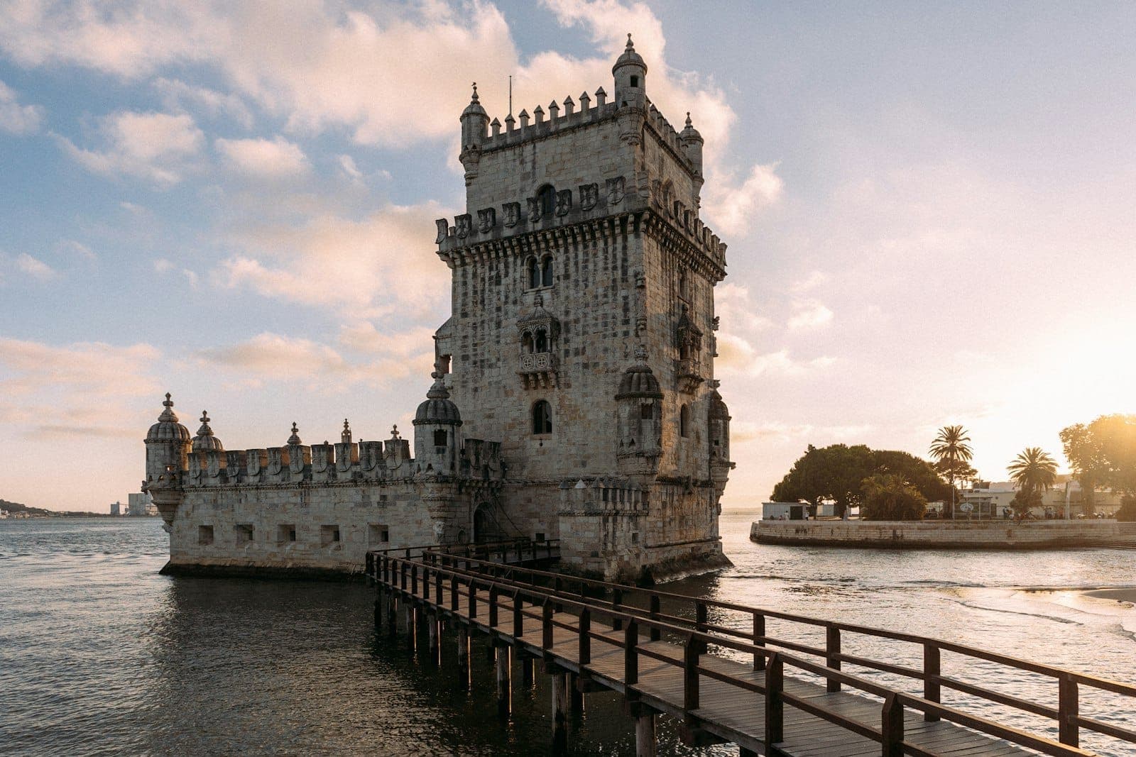 Torre de Belém, um importante monumento histórico à beira do rio em Lisboa, fotografada ao pôr do sol com uma passarela de madeira que leva à entrada.