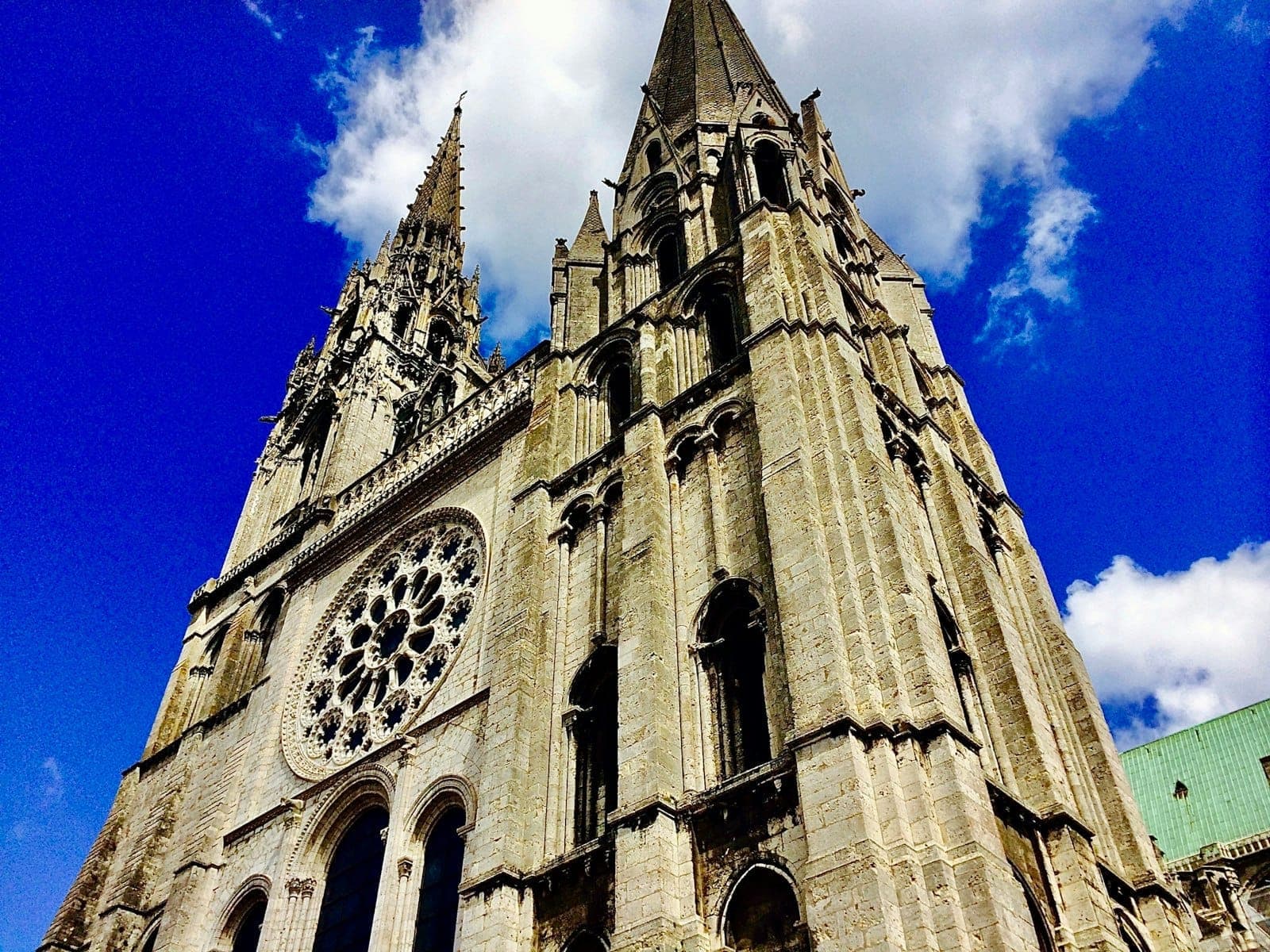 Vue spectaculaire en contre-plongée de la Cathédrale de Chartres avec ses deux flèches gothiques sur fond de ciel bleu et de nuages.