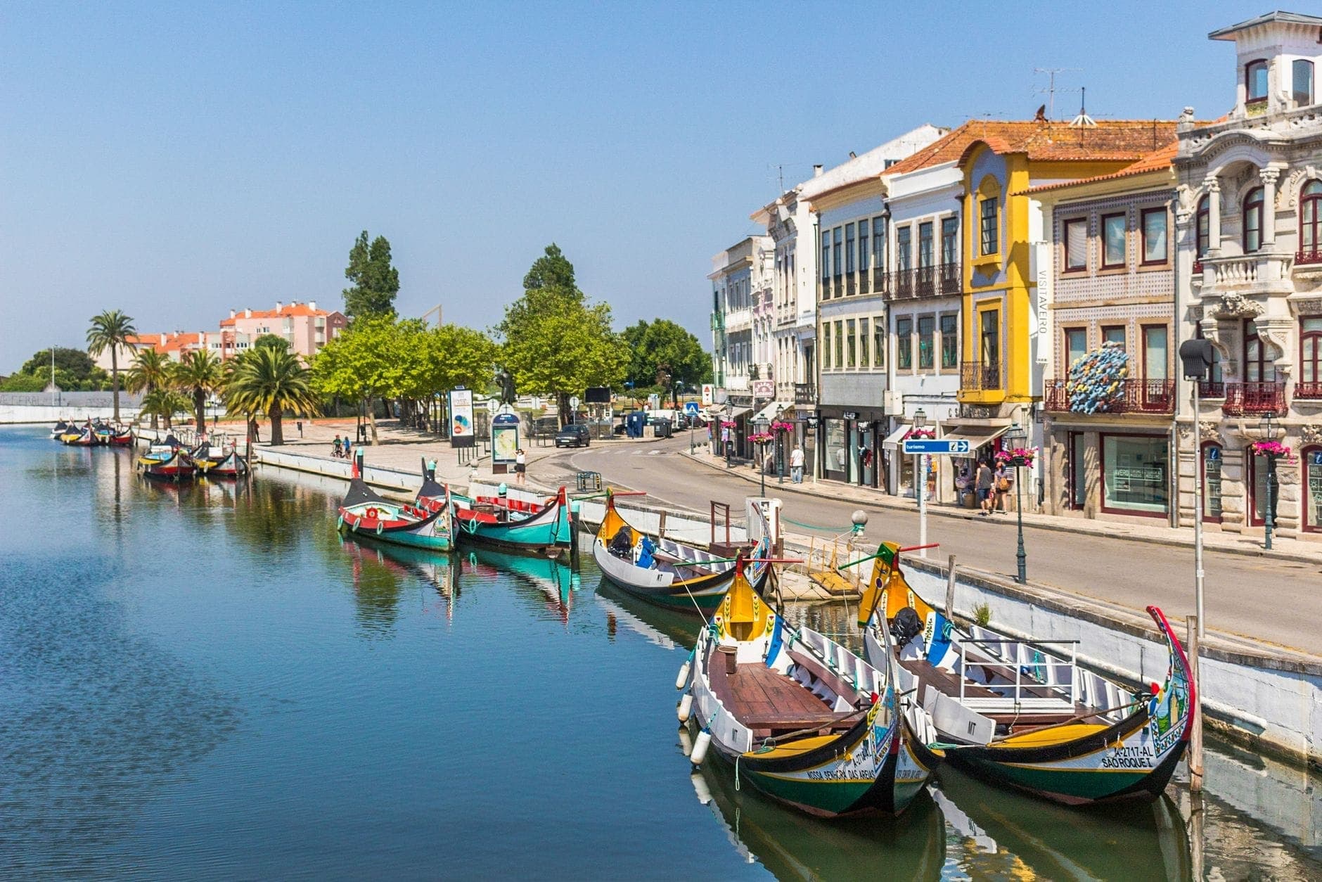 Portekiz'in Aveiro kentinde, güneşli bir günde Art Nouveau binalarıyla çevrili bir kanal boyunca demirlemiş renkli moliceiro tekneleri.