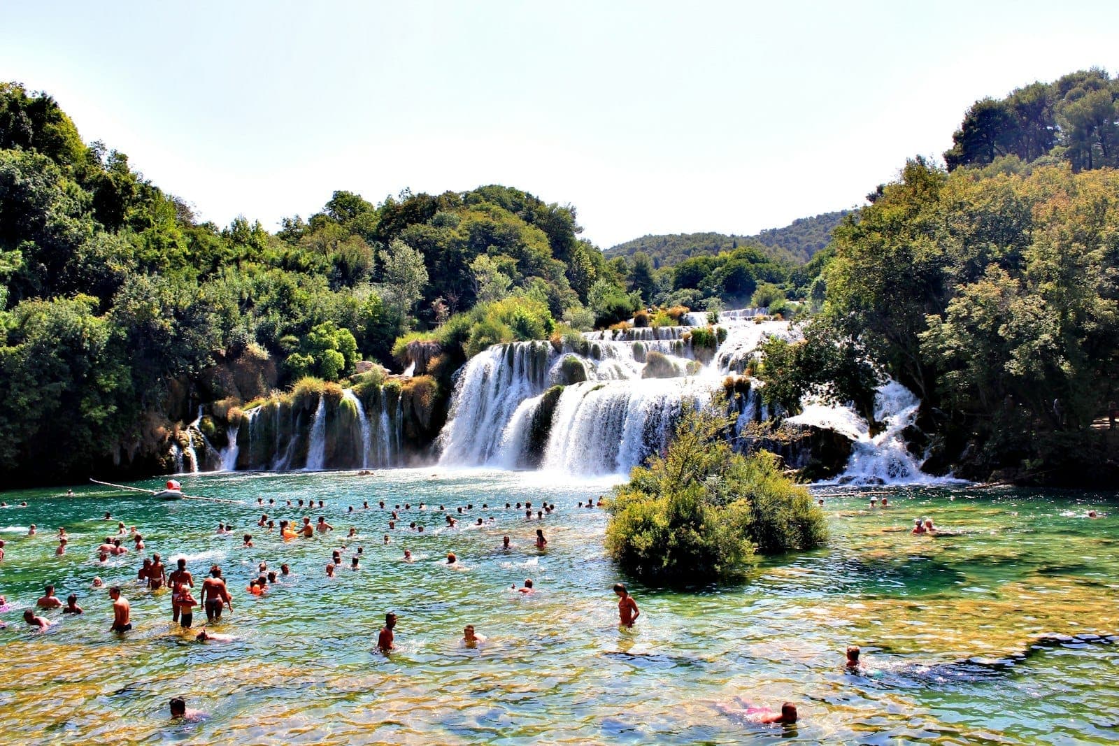 De nombreuses personnes nageant et pataugeant devant la cascade de Skradinski Buk au parc national de Krka par une journée ensoleillée.