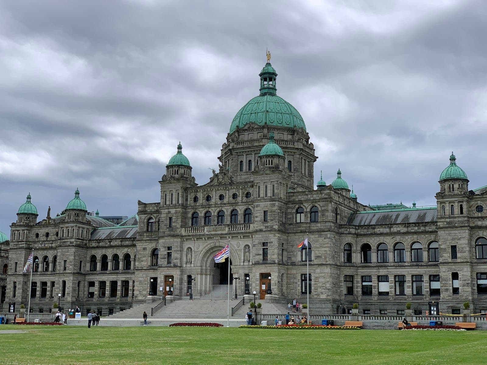 อาคารรัฐสภา British Columbia อันเก่าแก่ที่มีหลังคาโดมและสนามหญ้าด้านหน้า ภายใต้ท้องฟ้าครึ้มในเมืองวิกตอเรีย เกาะแวนคูเวอร์