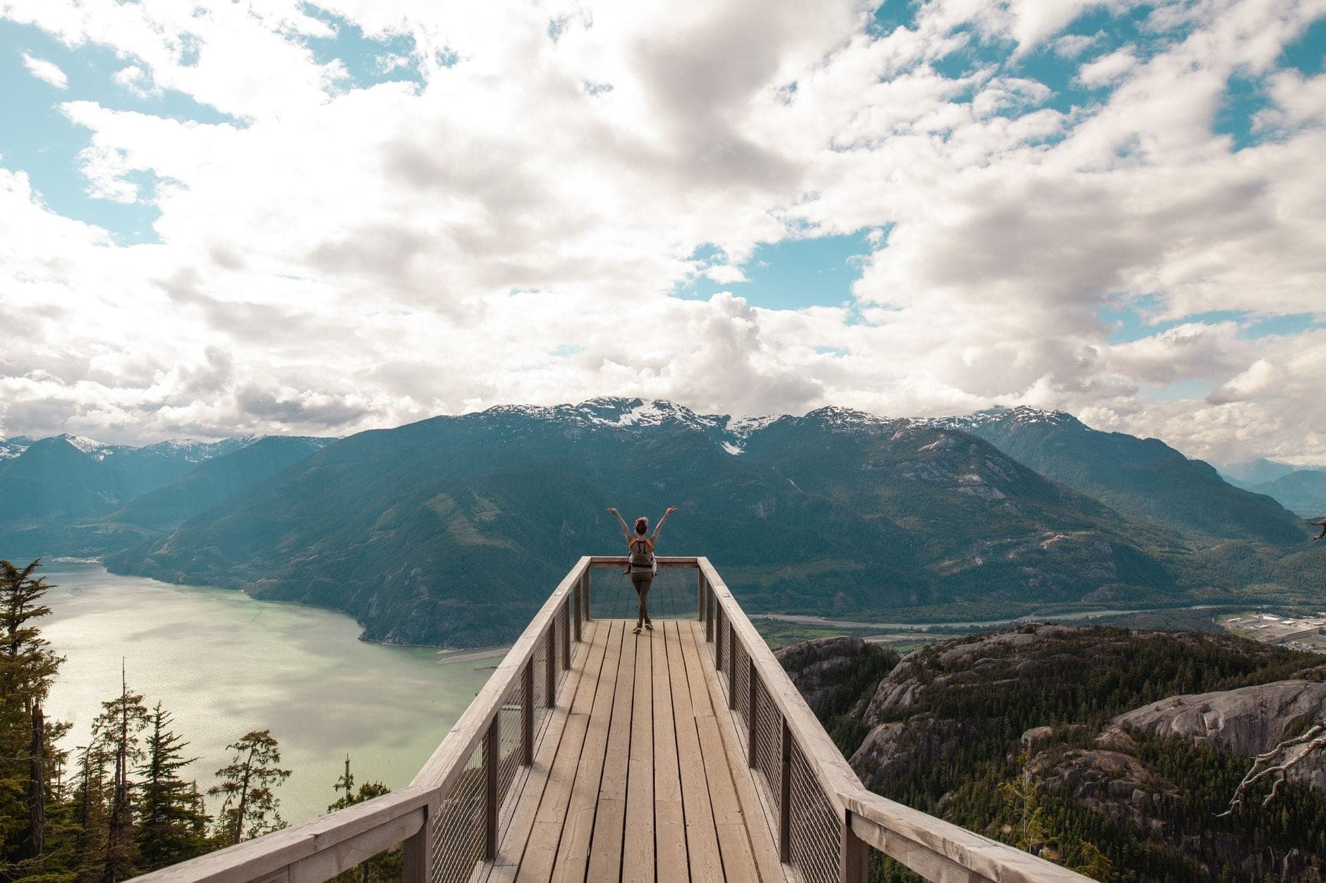 บุคคลยืนอยู่บนจุดชมวิวที่มองเห็น Howe Sound และเทือกเขาบน Sea-to-Sky Highway ใกล้ Squamish