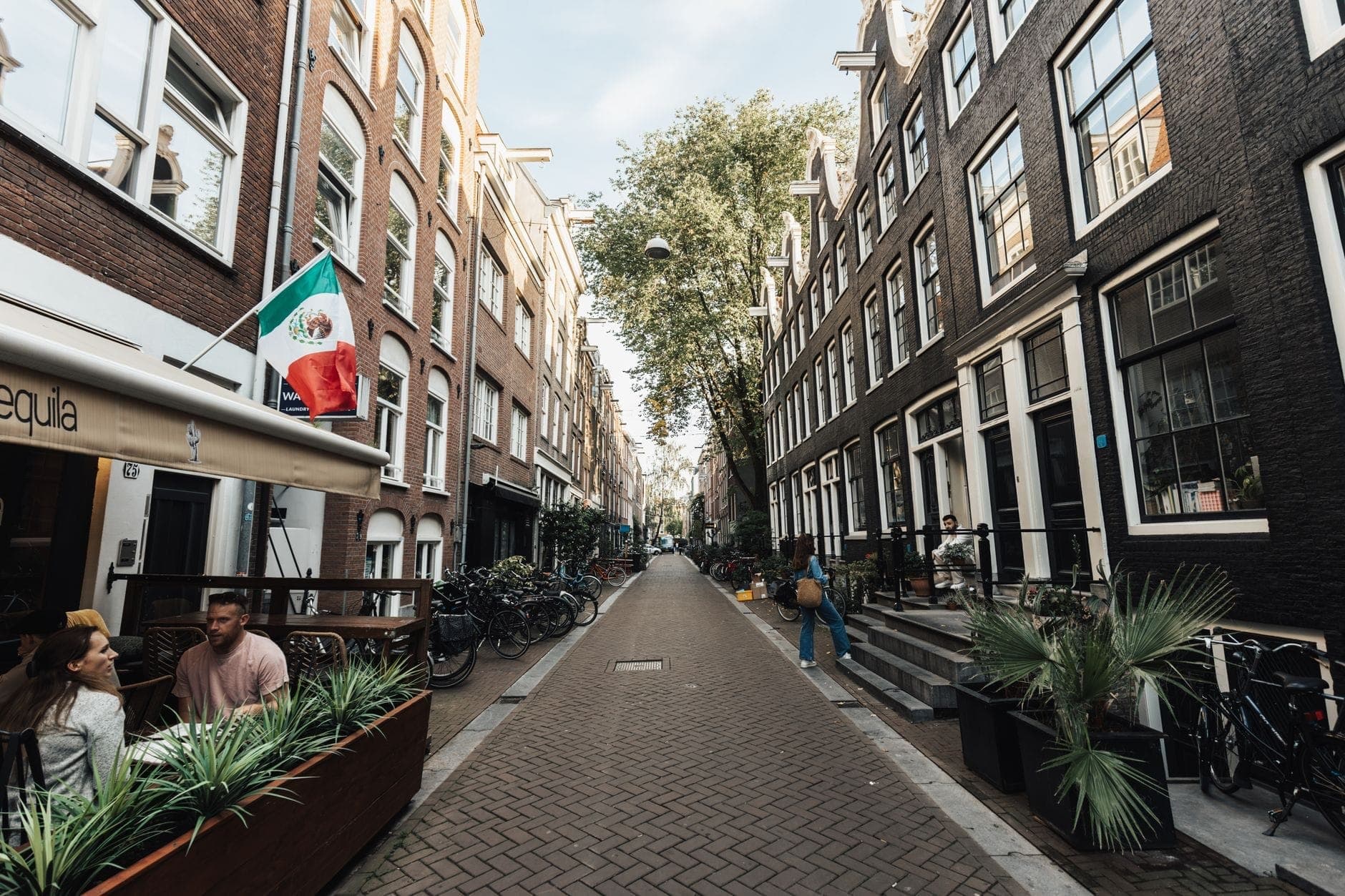 Charmante Amsterdamer Straße in De Negen Straatjes mit historischen Gebäuden, Caféterrassen, Fahrrädern und grünen Bäumen – eine Einladung zum entspannten Flanieren.