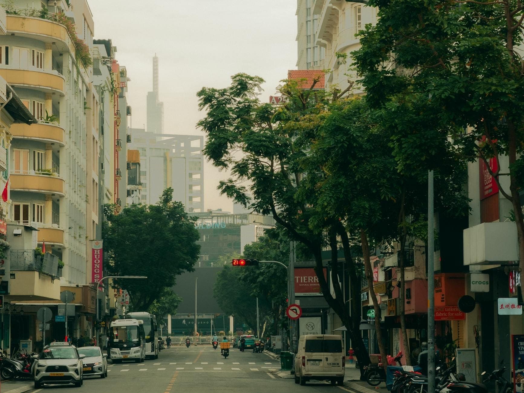 ถนนร่มรื่นในเขต 3 นครโฮจิมินห์ บรรยากาศสงบยามบ่าย มีอาคารสไตล์โคโลเนียลฝรั่งเศส ร้านค้าริมทาง และรถมอเตอร์ไซค์วิ่งผ่านไปมา