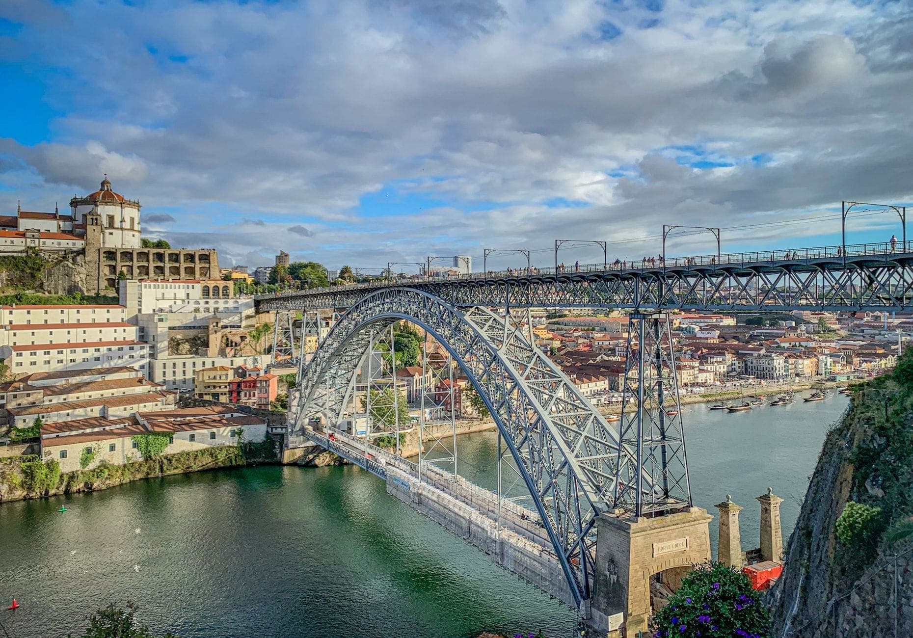 Le pont Dom Luís I arqué au-dessus du Douro, reliant les bâtiments historiques colorés de Porto et de Vila Nova de Gaia sous un ciel dramatique.
